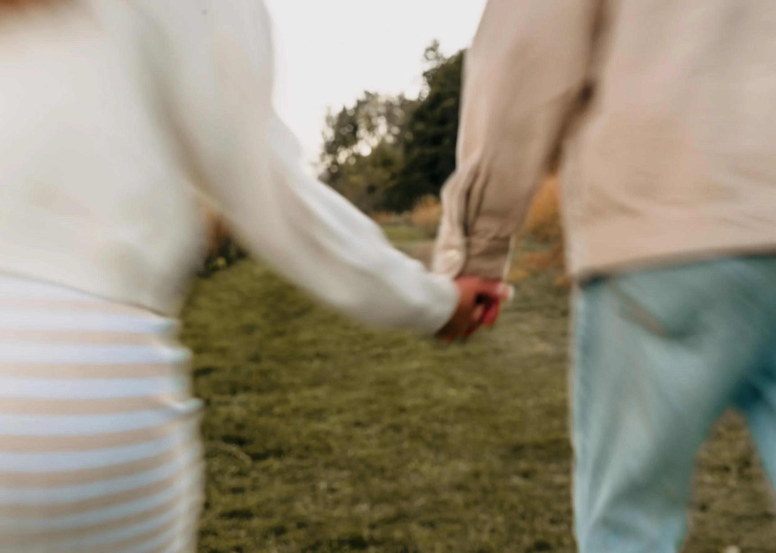 Close-up shot of a couple holding hands outdoors, with a blurred background of trees and grass.