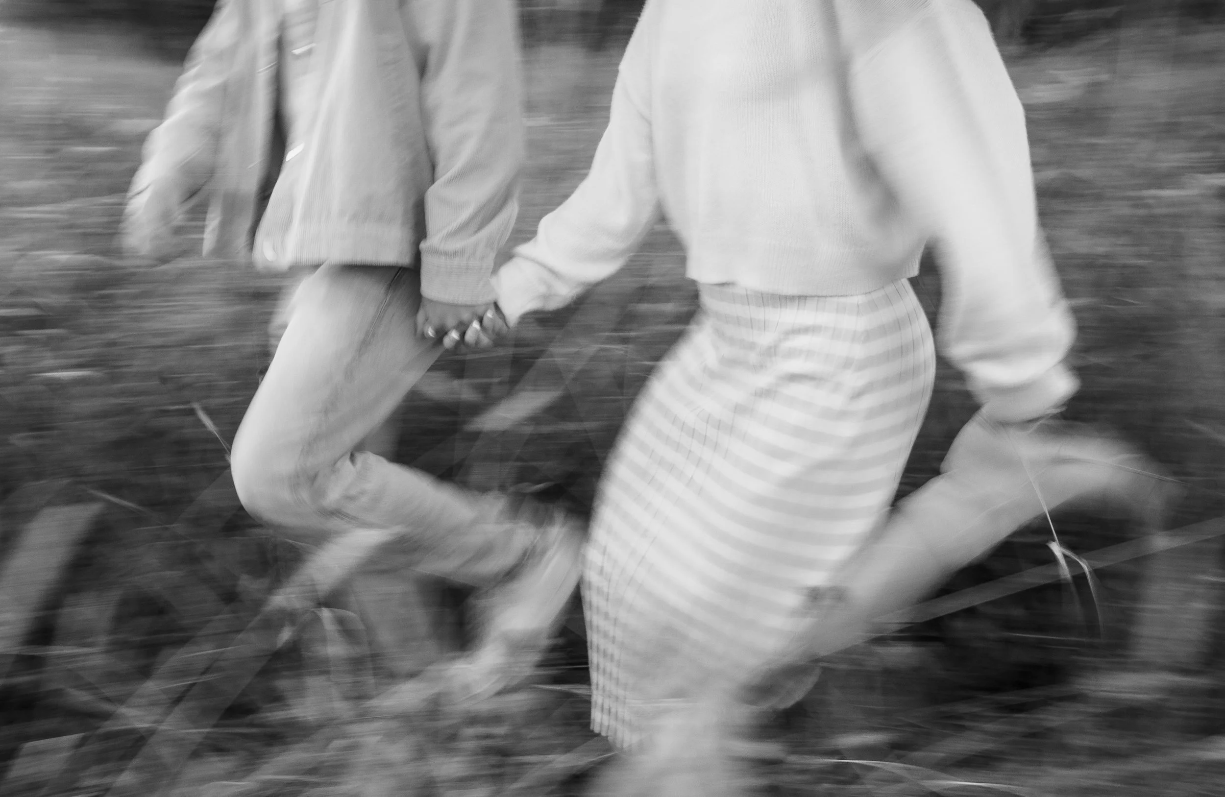 Two people holding hands while running outdoors, with a blurred background.