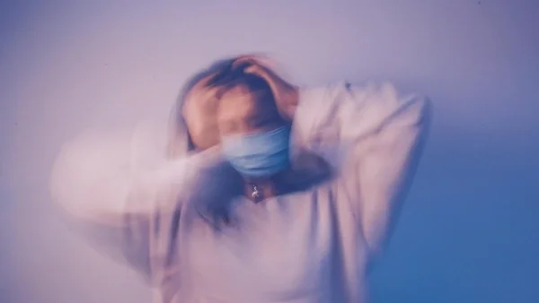 Blurred image of woman with hands on head and surgical mask on face