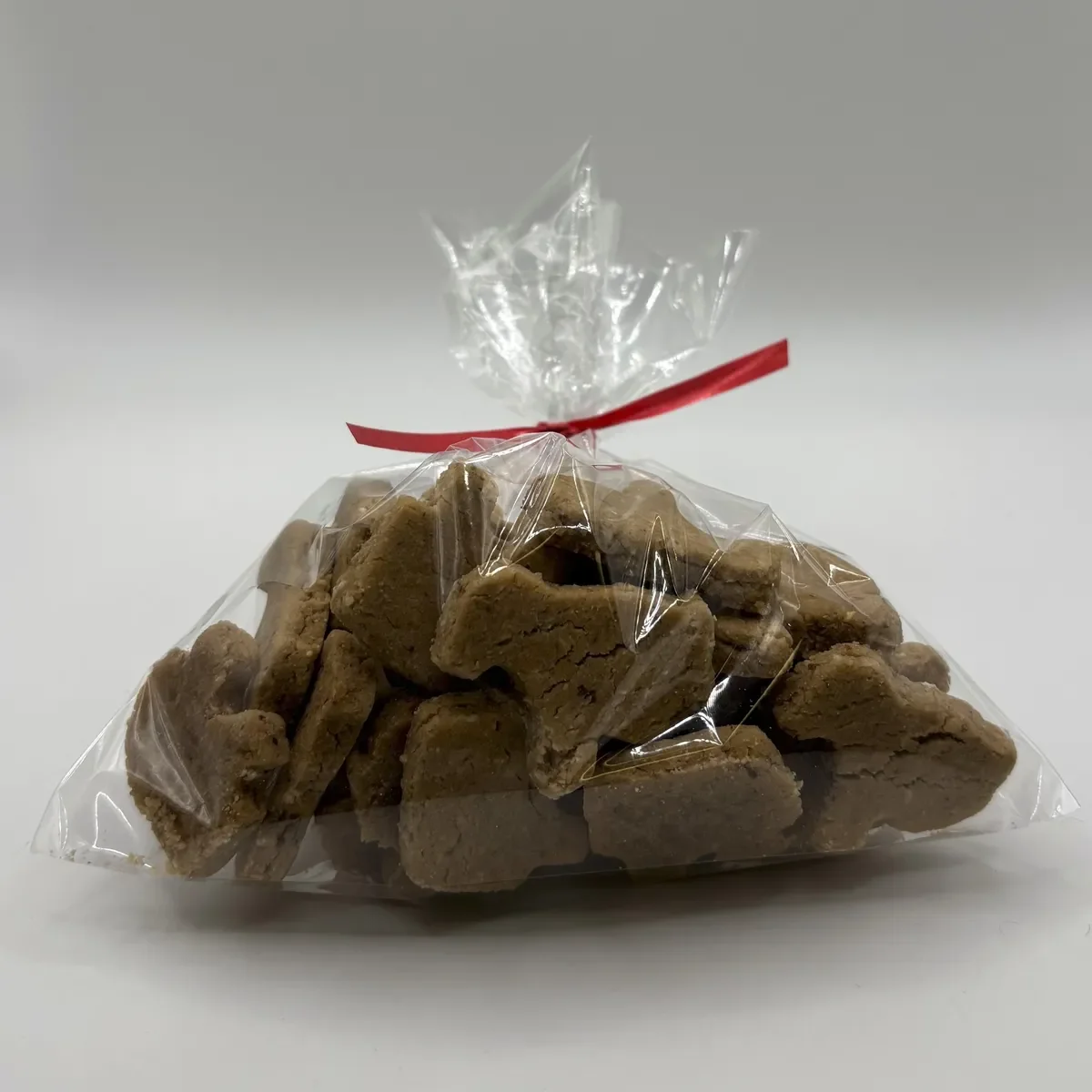 A clear plastic bag tied with a red ribbon, filled with bone-shaped brown dog treats, on a white background.