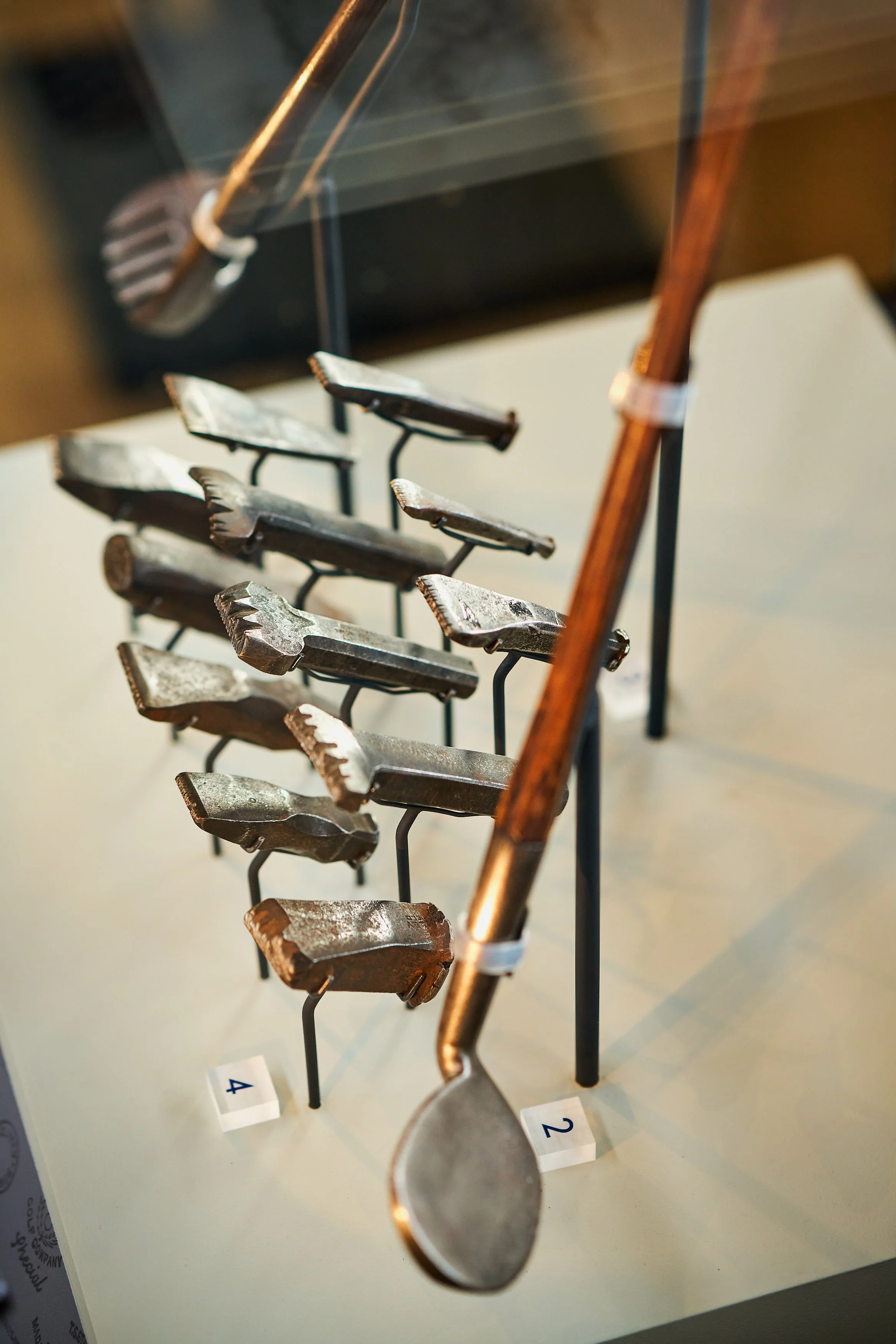 A display of historic golf clubs, arranged on small stands with numbered labels.