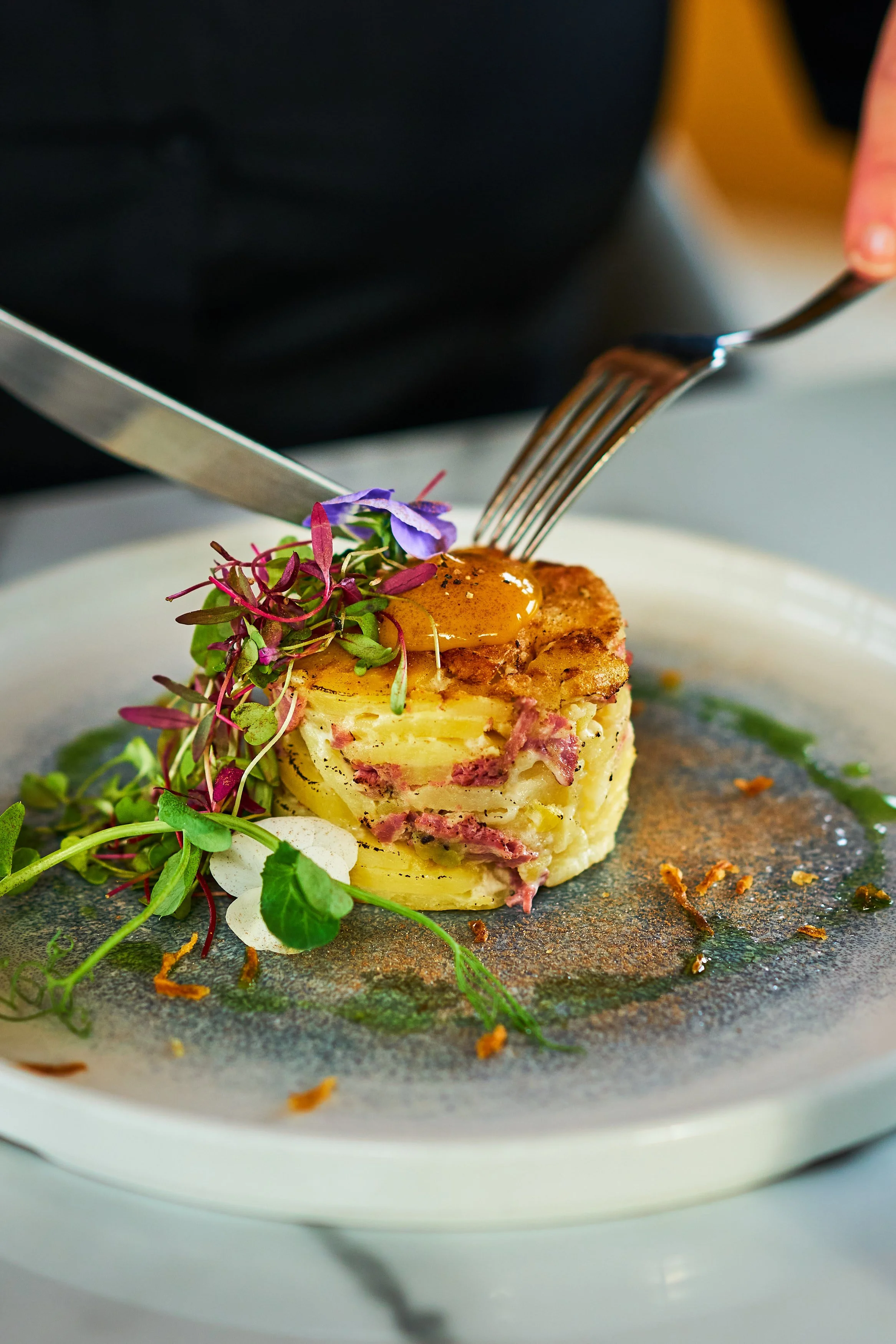 A plated serving of potato au gratin with a poached egg, garnish of microgreens, and edible flowers.
