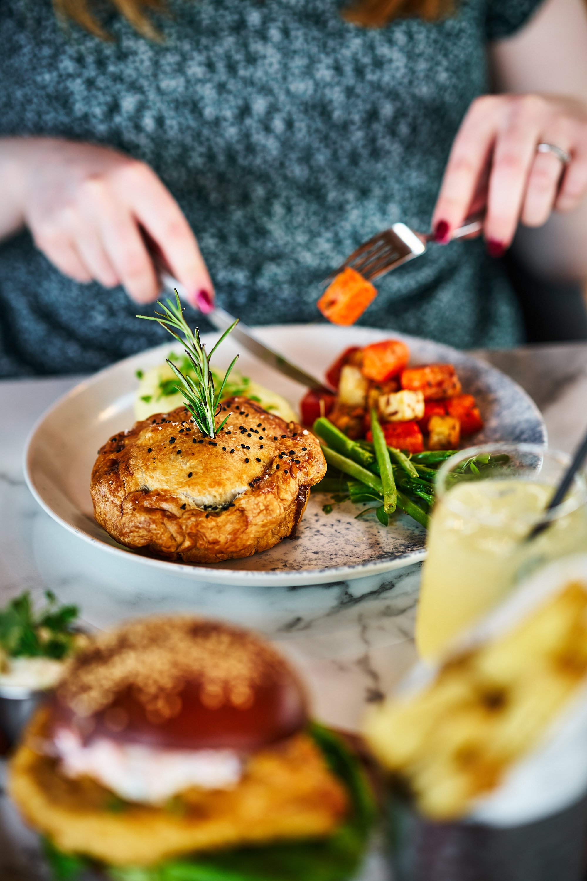 A diner slices into a pile of vibrant vegetables served alongside a freshly cooked pie.