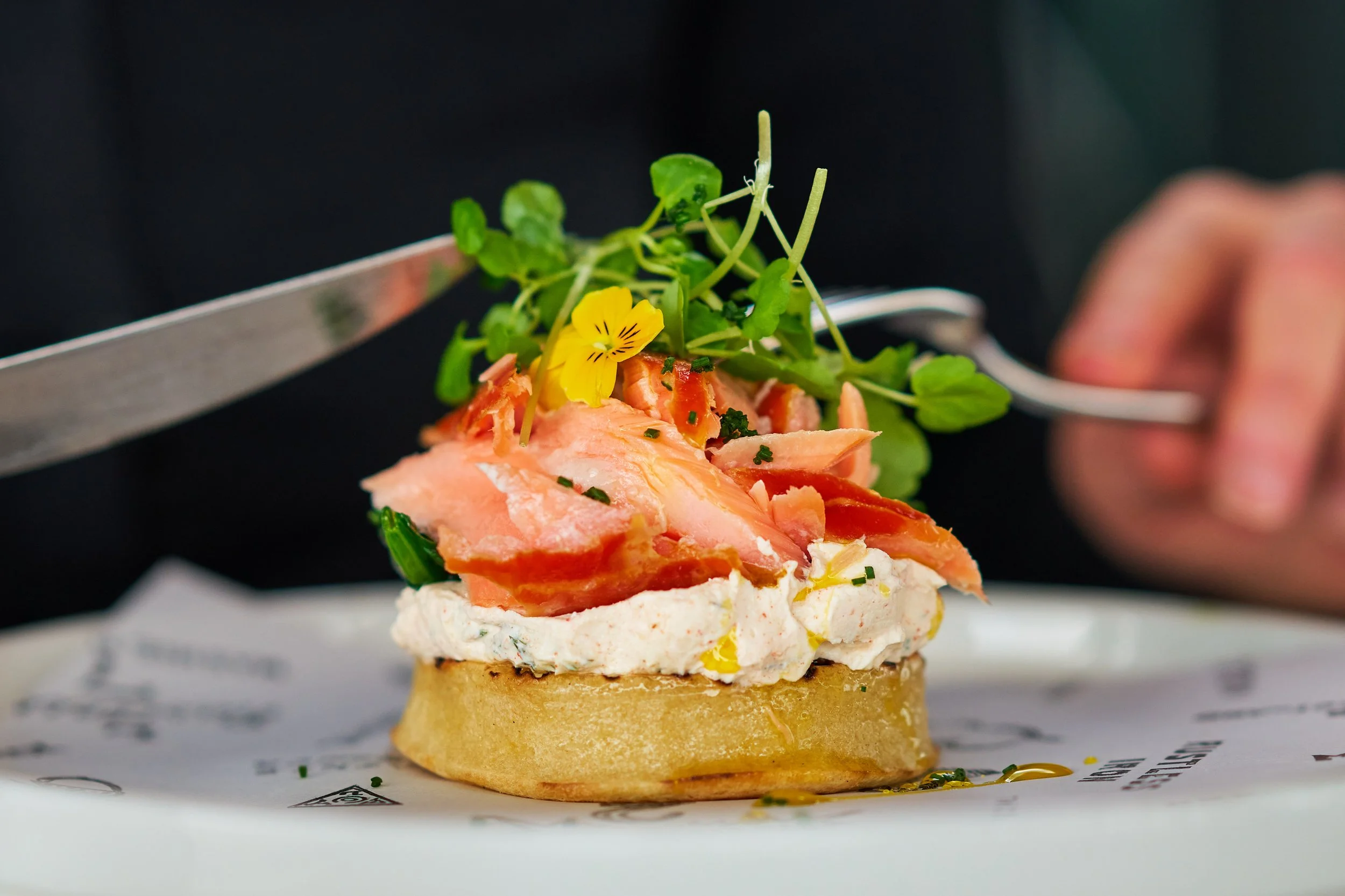 Close-up of an scone with smoked salmon, a creamy spread, microgreens, and edible flowers.
