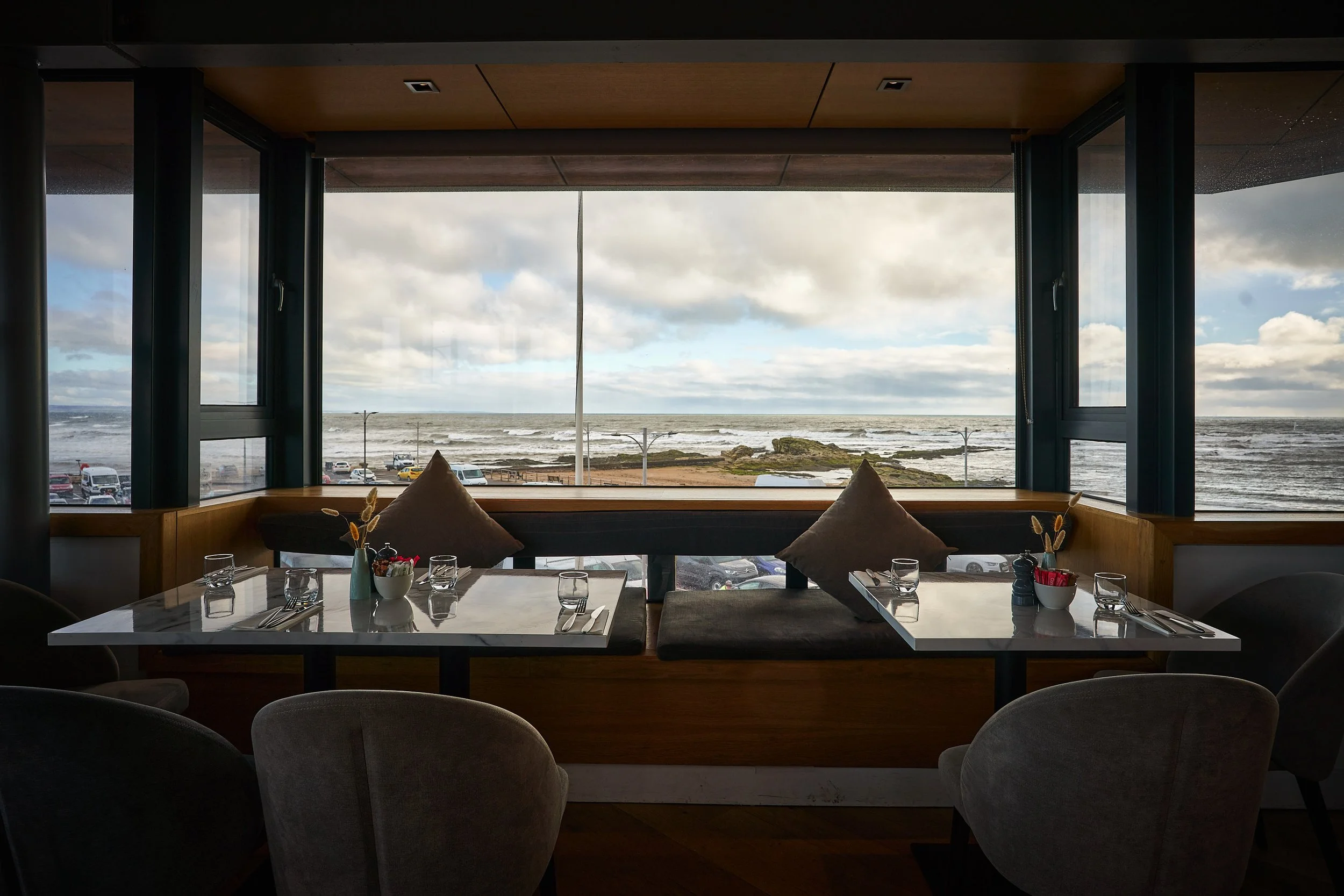 A table set for diners sits by a window offering a stunning view of the North Sea in St Andrews. Comfortable seats surround the table, creating an inviting atmosphere.