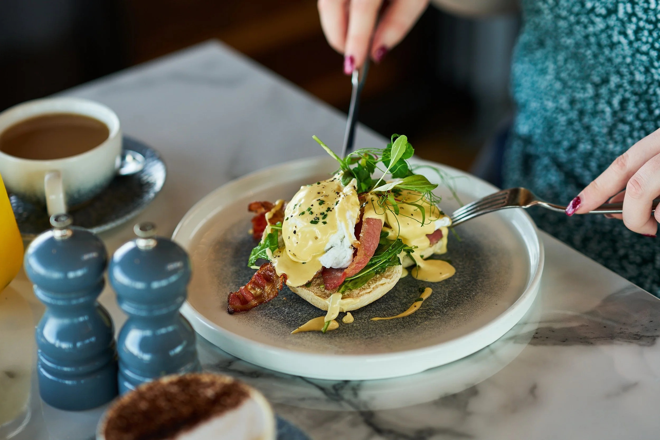 A generous serving of eggs benedict is plated alongside a steaming cup of coffee.