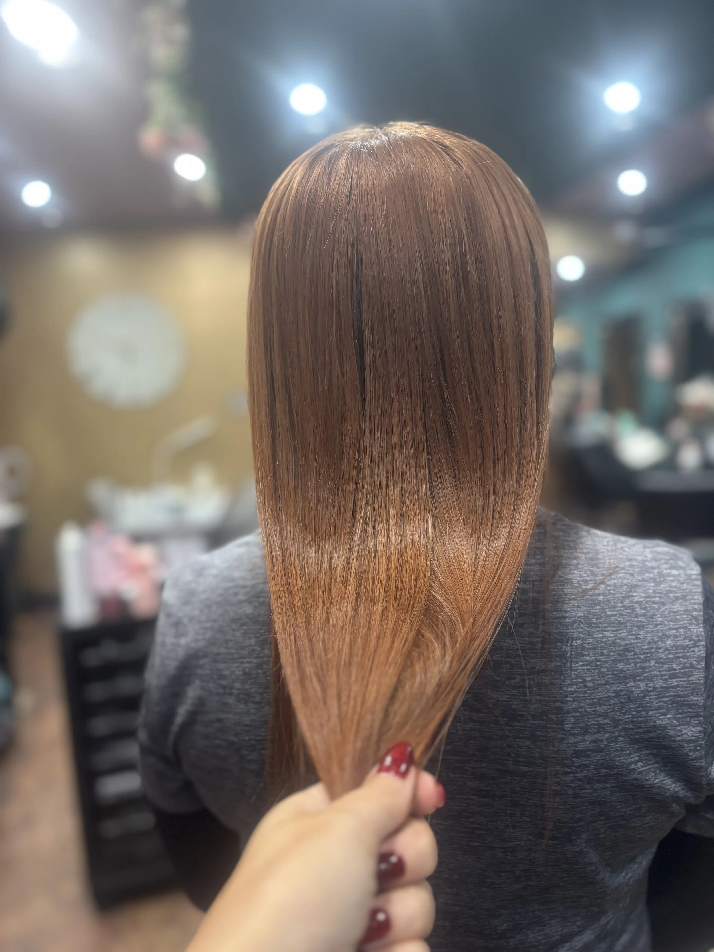 A person with freshly dyed straight hair in a salon, held by a hand with red nail polish.