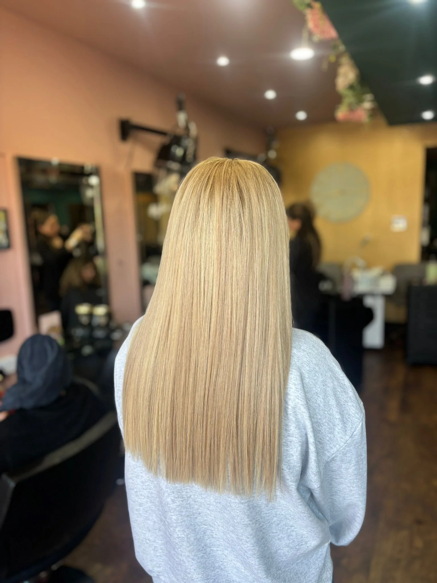Back view of a woman with long, straight, blonde hair inside a salon.