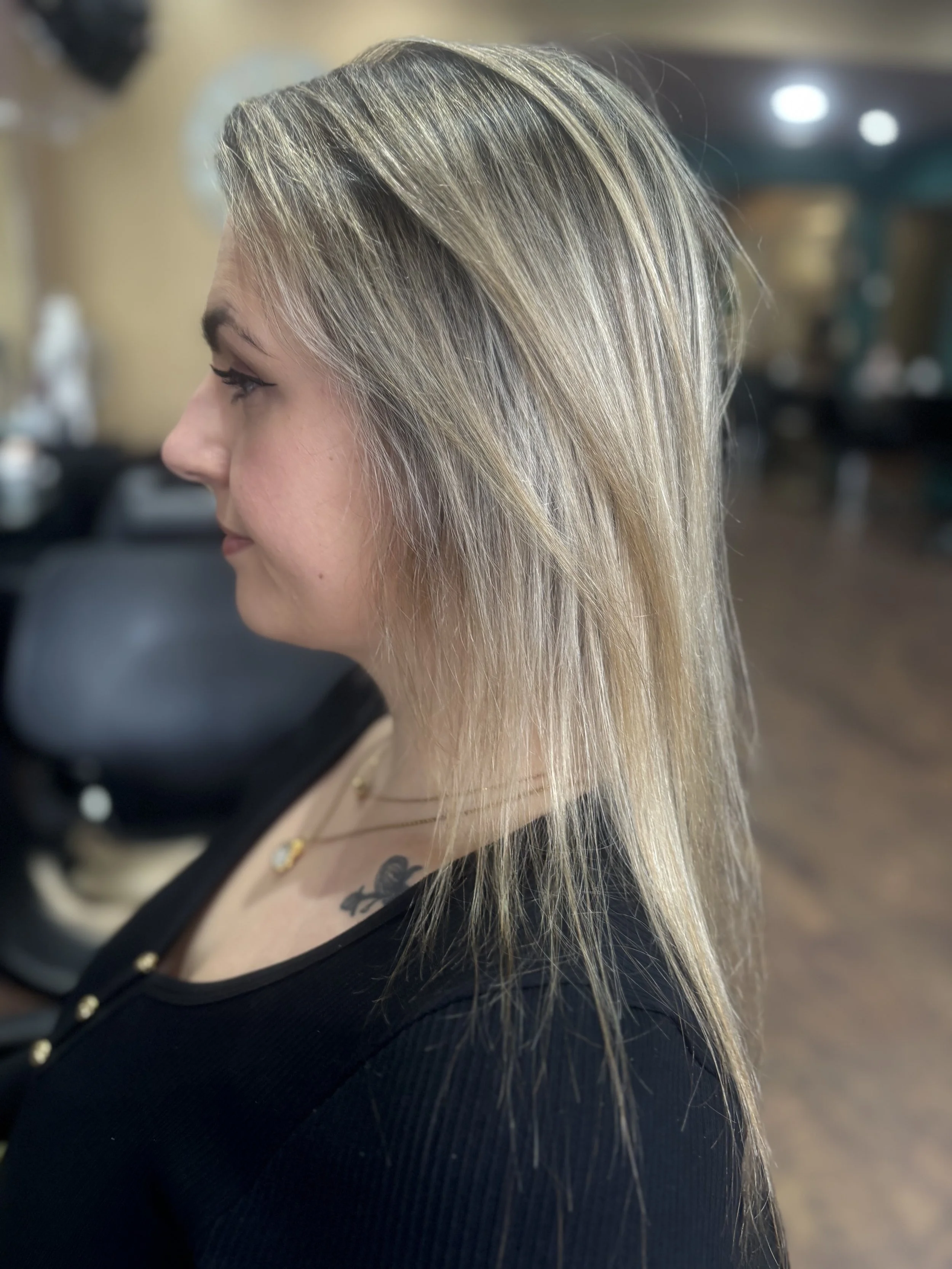 Side profile of a woman with straight, shoulder-length blonde hair, sitting in a salon.