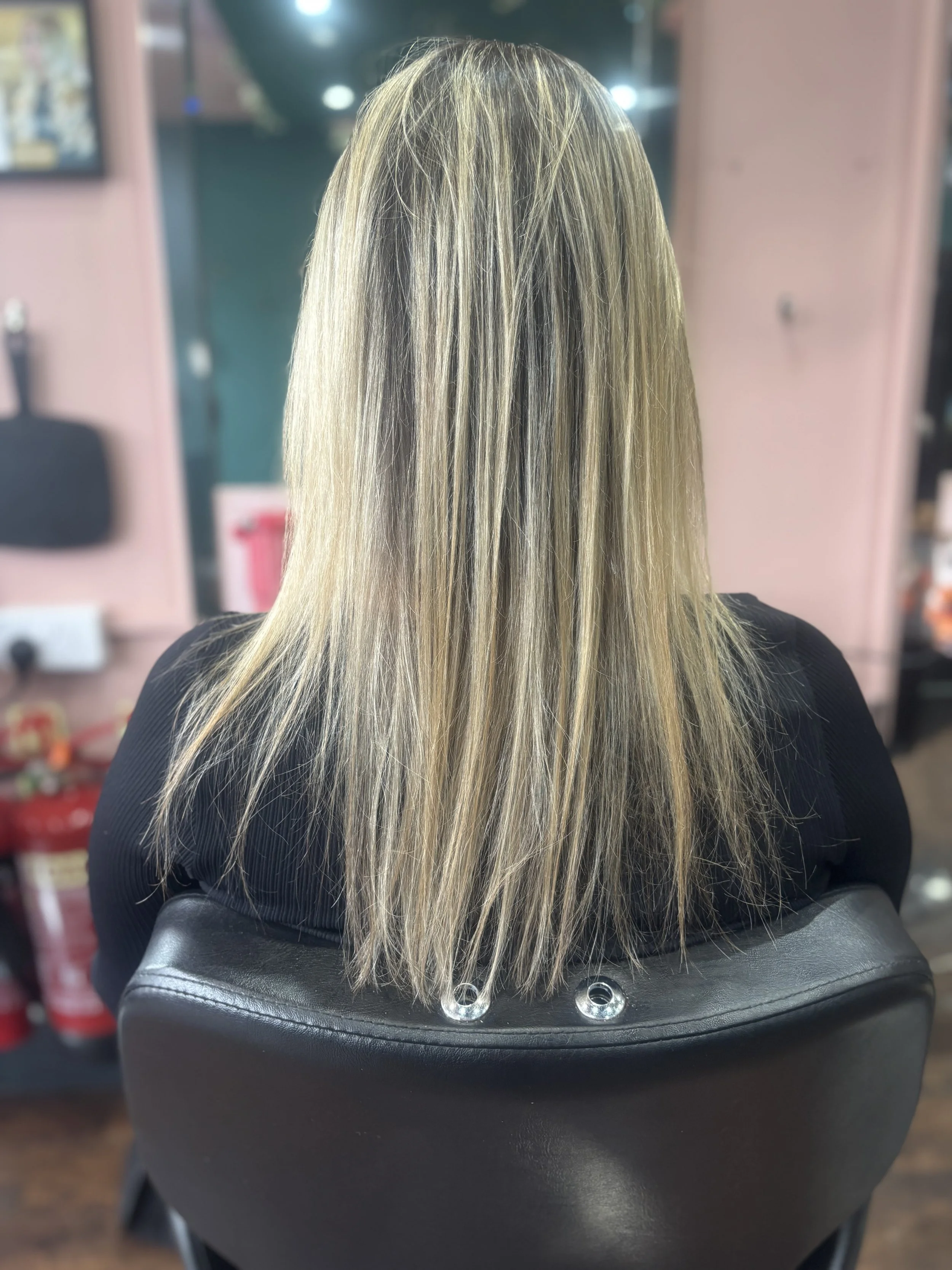 Back of a woman with blonde, straight hair sitting in a salon chair in a hair salon.