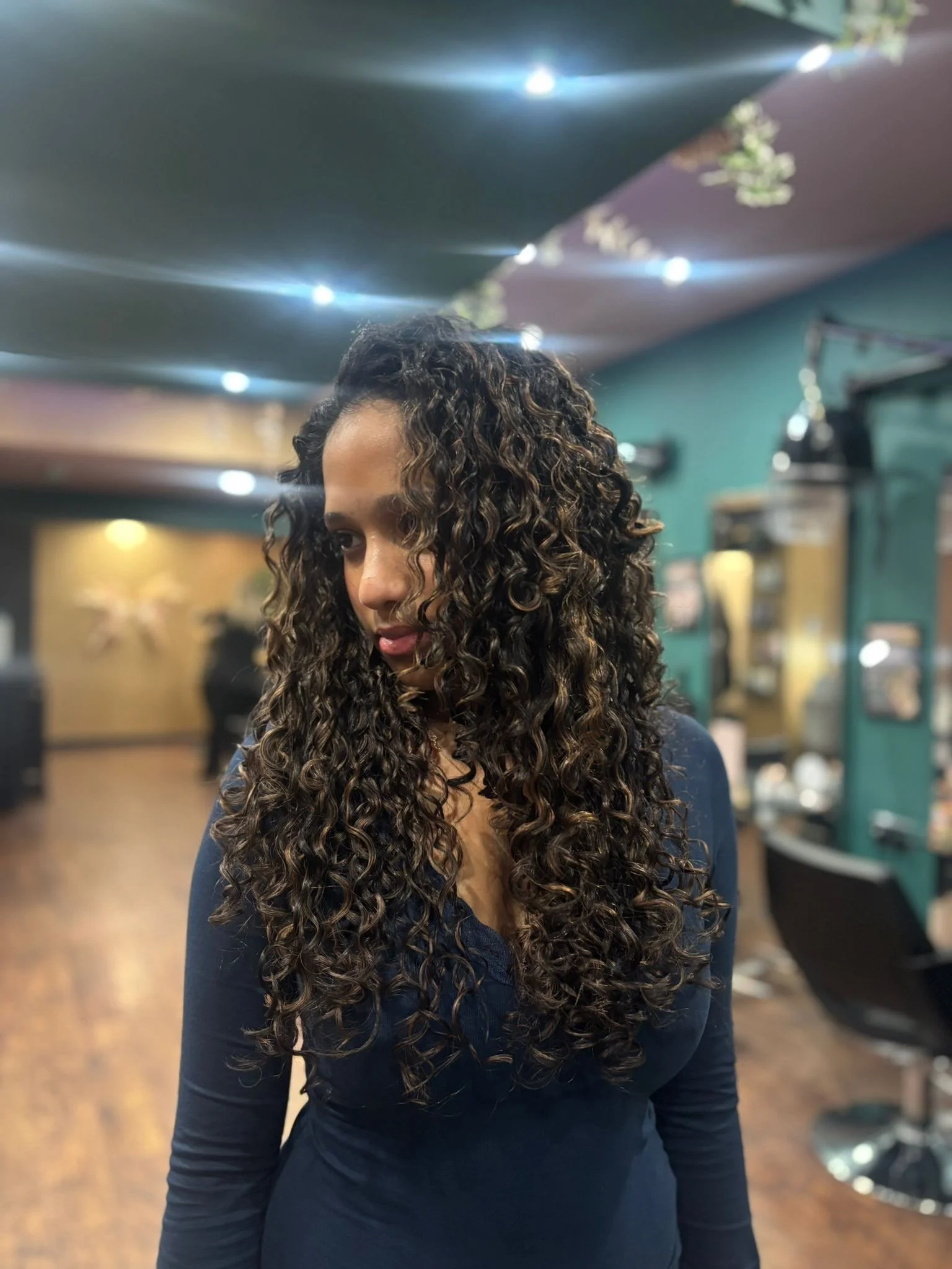 Woman with long, dark, curly hair looking down inside a salon.