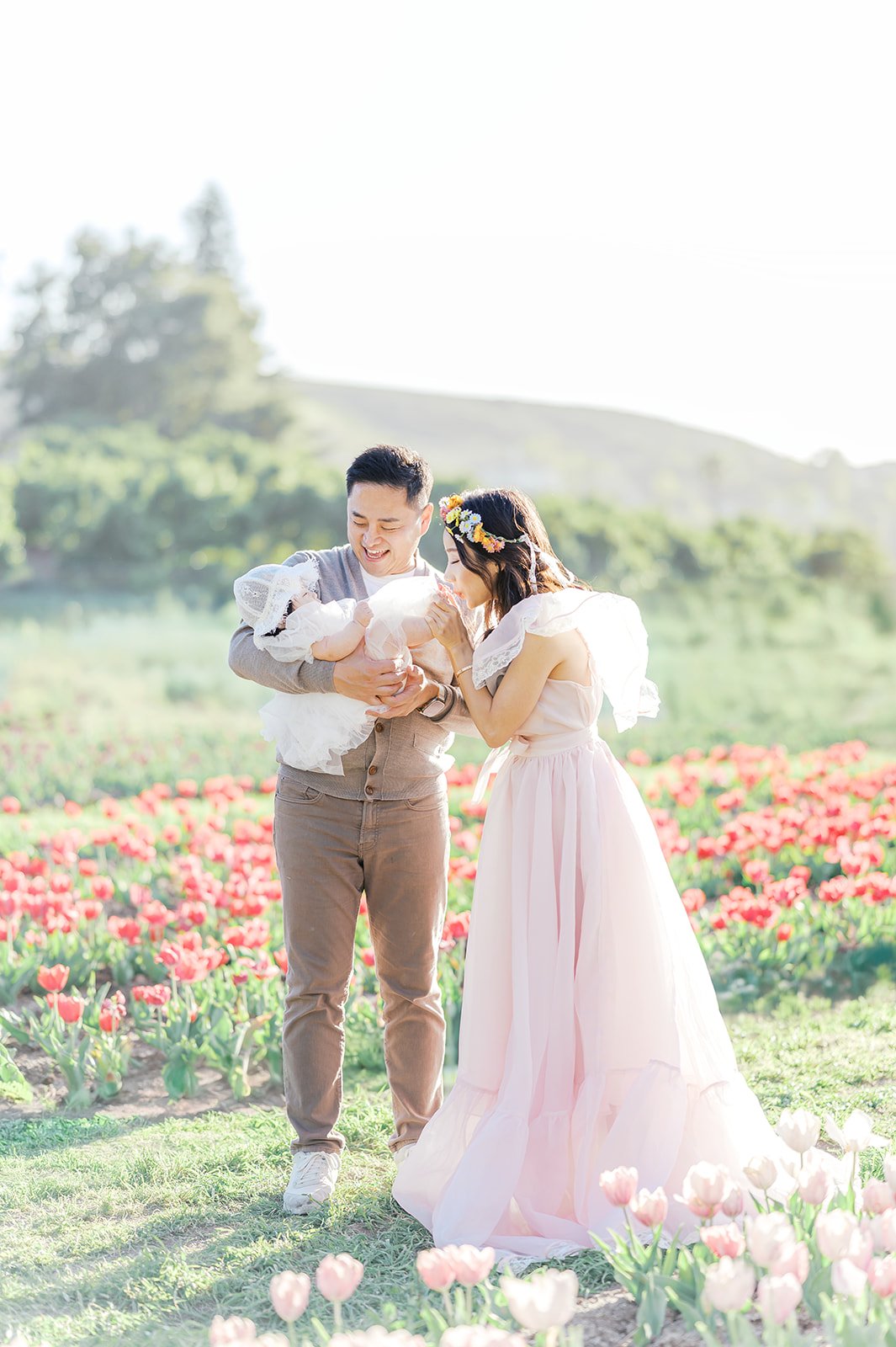 Tulip family photos of parents holding their baby while walking together through a blooming tulip field in spring.