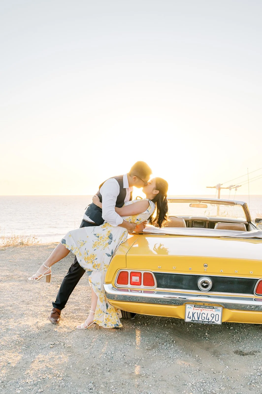 Summer Engagement Photos in Malibu featuring a couple kissing beside a vintage yellow Ford Mustang convertible overlooking the Pacific Ocean at sunset.