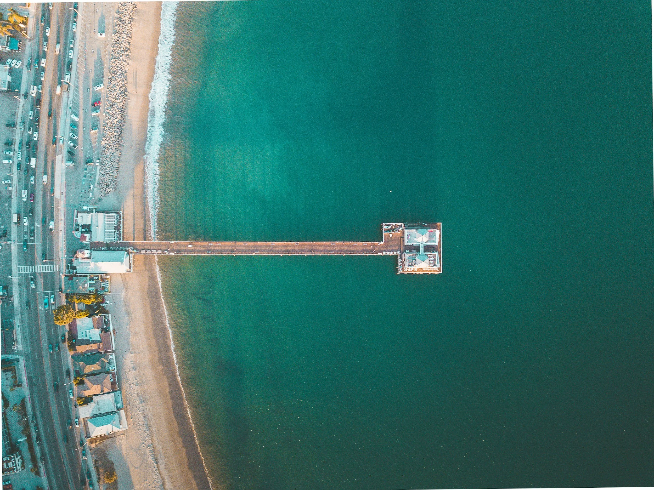 Ariel view of the Malibu Pier with emerald green ocean water and a busy PCH