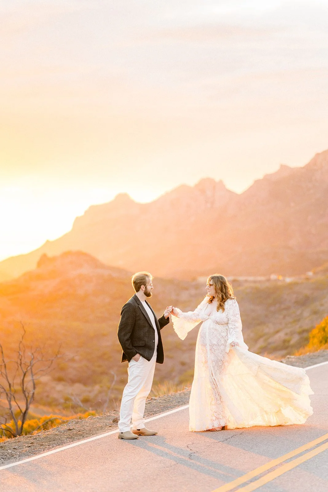 Summer Engagement Photos in Malibu featuring a couple holding hands on a scenic Santa Monica Mountains road surrounded by golden sunset light.
