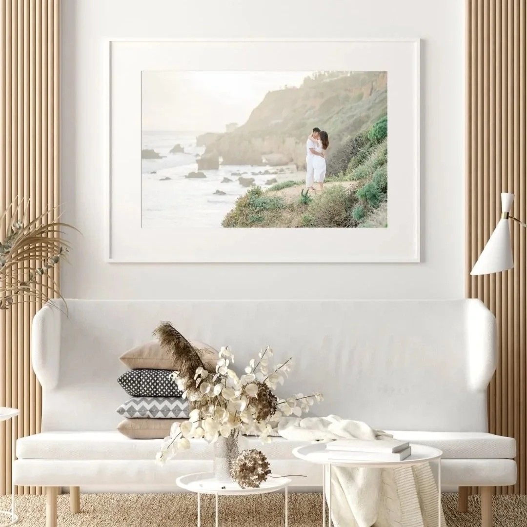 El Matador Beach Engagement Photos displayed as a large framed heirloom print in a bright, modern coastal living room with neutral décor and elegant white matting.