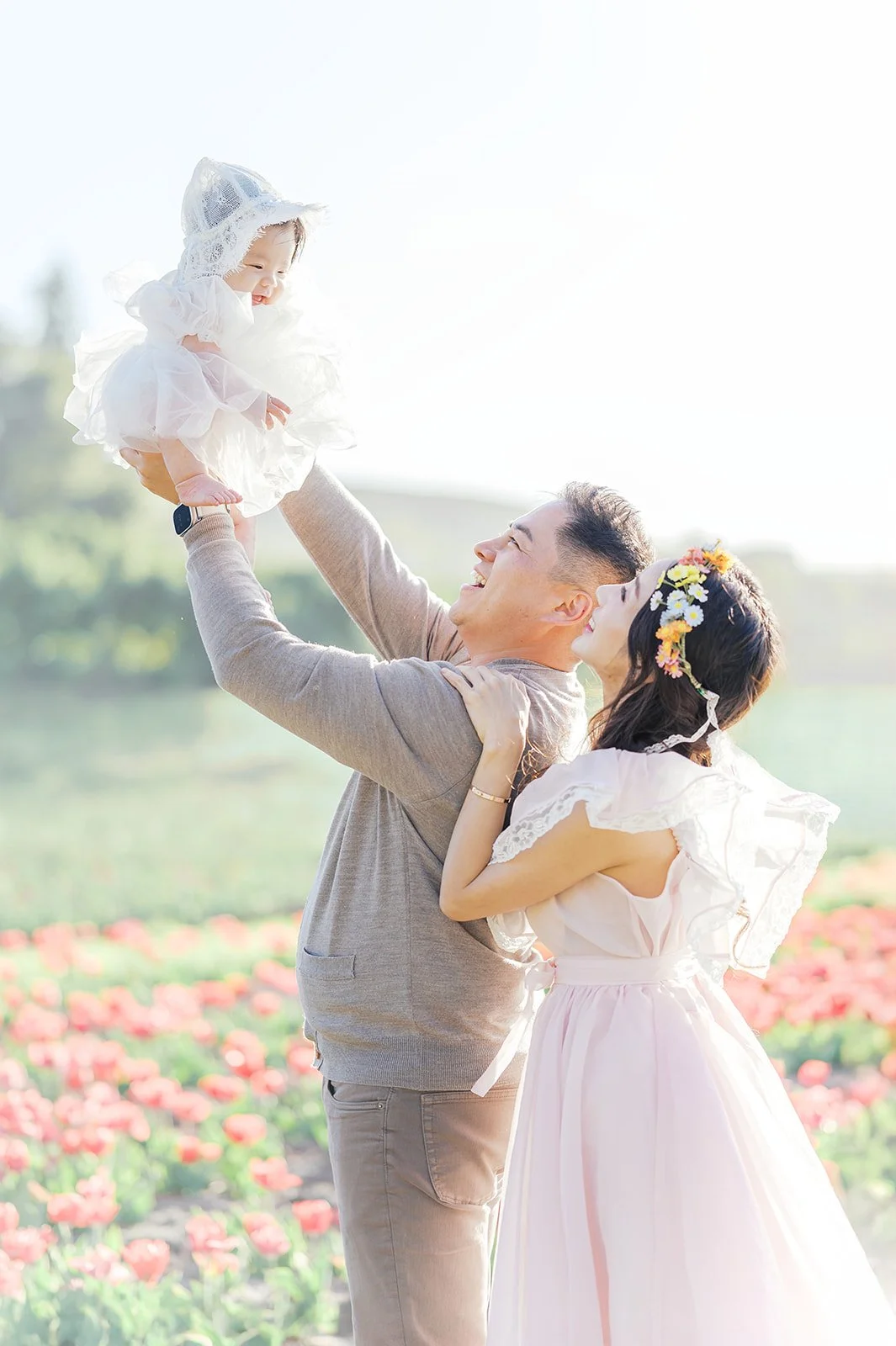 Tulip family photos of parents lifting their baby into the air while standing in a spring tulip field.