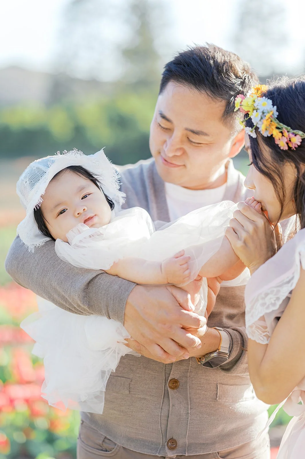 Tulip family photos of parents holding their baby close during a spring photoshoot in a blooming tulip field.