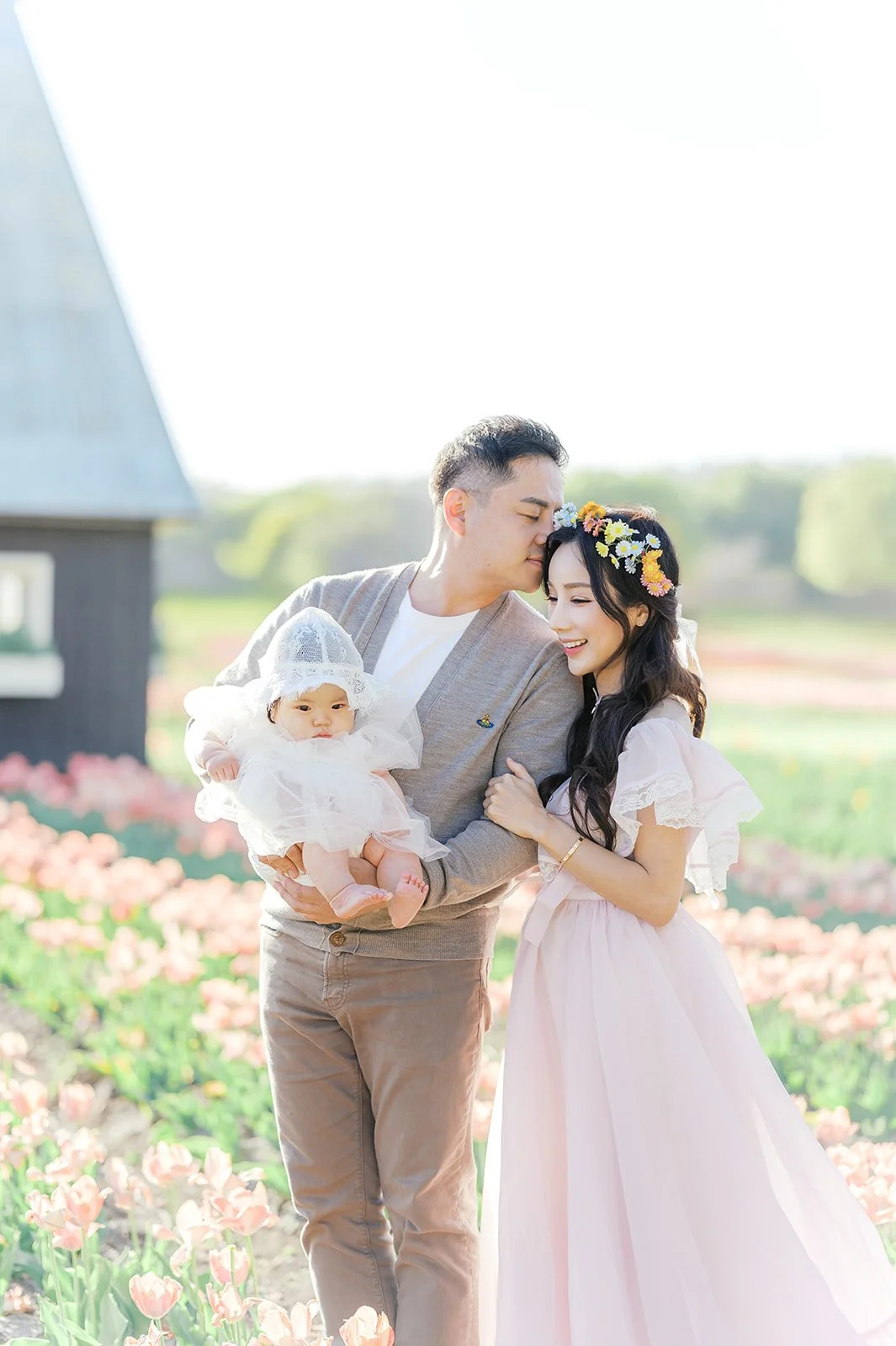 Tulip family photos of parents holding their baby while walking through a blooming pink tulip field in spring.
