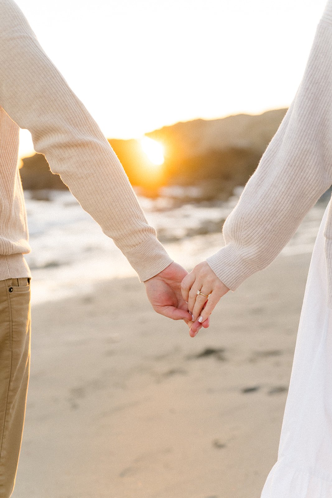 Summer Engagement Photos in Malibu featuring a close-up of a couple holding hands and showing an engagement ring as the sun sets over the beach.