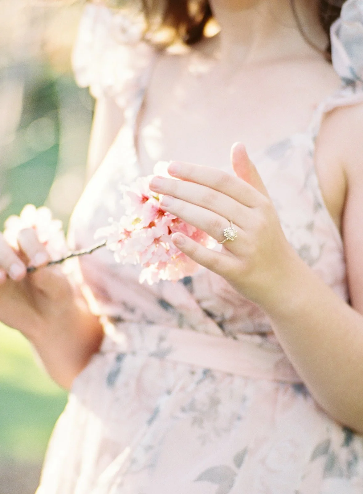 Cherry Blossom Photoshoot ideas featuring a close-up of hands gently holding a cherry blossom branch, with soft pink petals and a delicate ring highlighted in warm, glowing sunlight