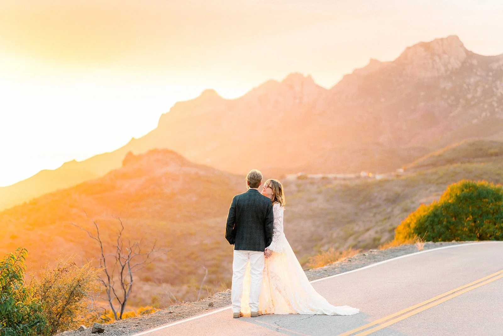 Summer Engagement Photos in Malibu featuring a couple standing together on a winding mountain road surrounded by the Santa Monica Mountains at golden hour.
