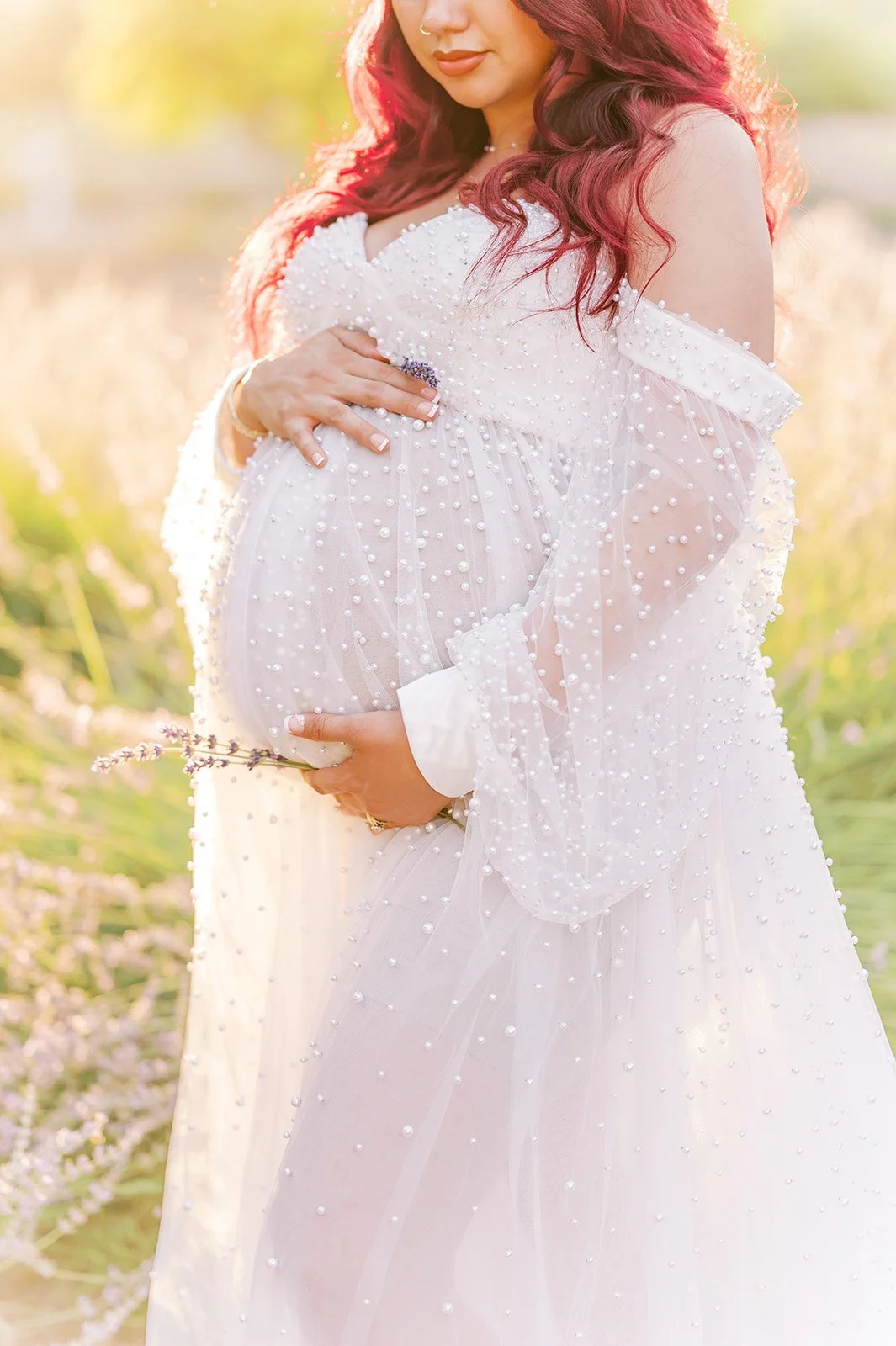 Summer Maternity Photos of an expecting mother in a flowing pearl-detailed gown standing in a lavender field during warm golden hour light.