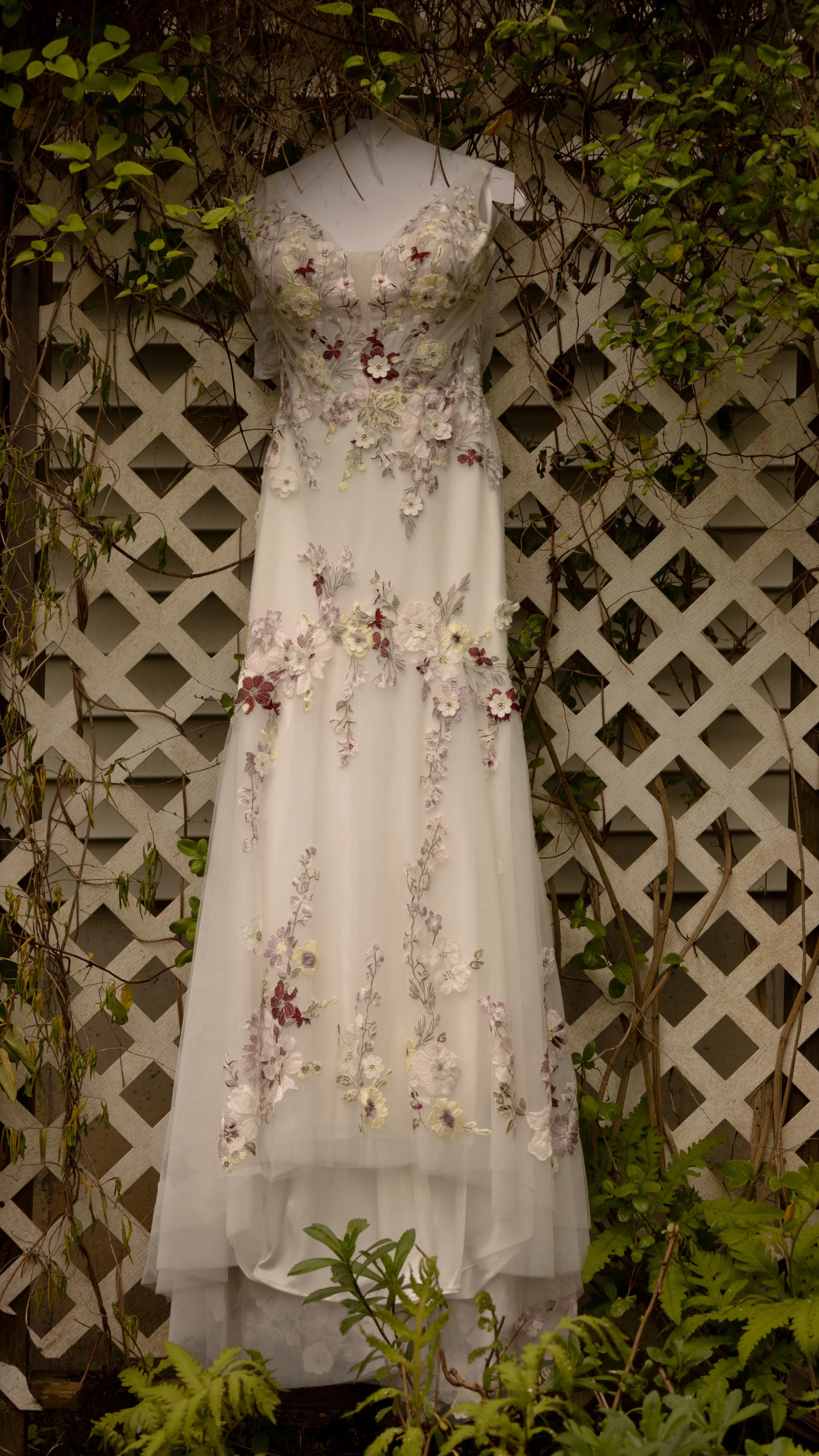 Wedding dress with floral embroidery hanging on a wall surrounded by green plants and vines. Hamptons elopement photographer. Hamptons wedding photographer. Shelter island wedding photographer. 