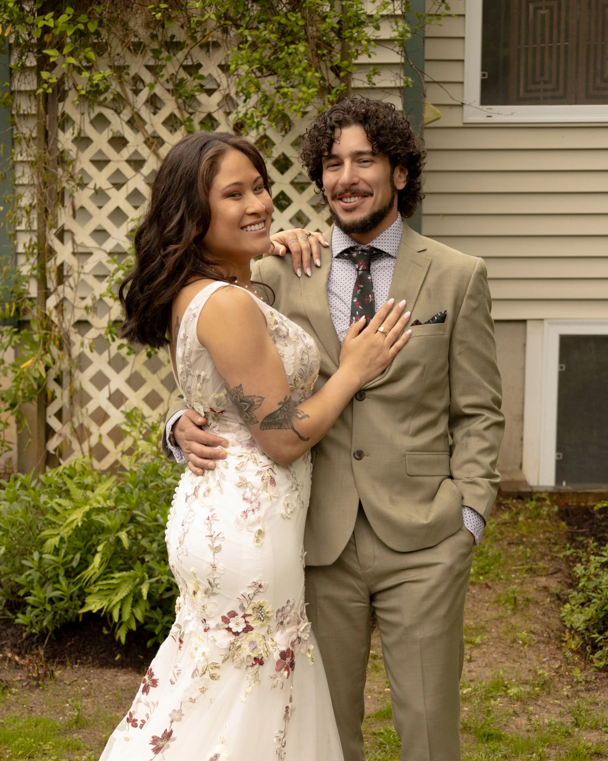 A smiling backyard wedding couple embracing outdoors near a house with  timeless Long Island wedding photography. 