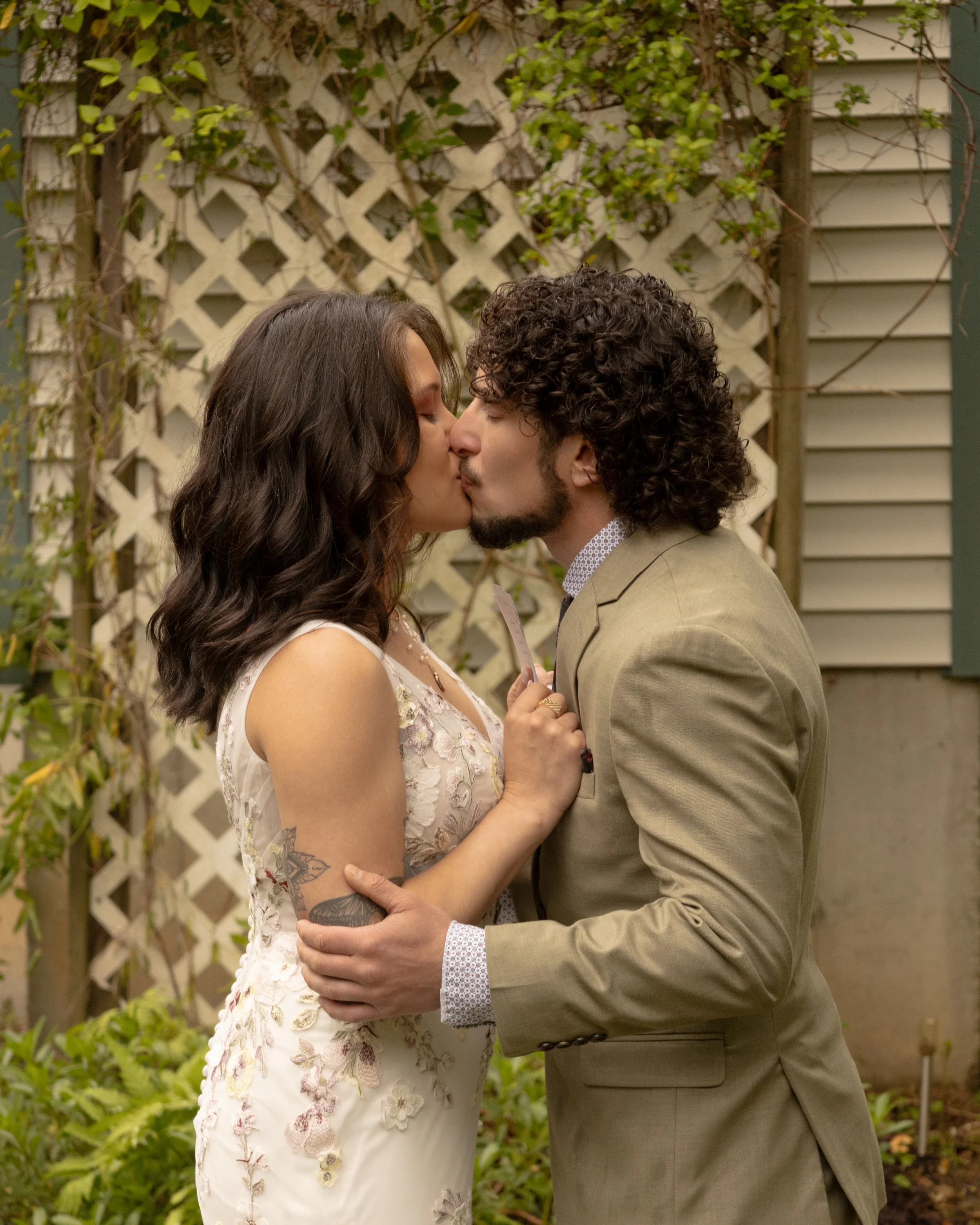 A couple kissing outdoors in front of a garden with lattice and green plants. Hamptons elopement photographer. Shelter Island Wedding Photographer.