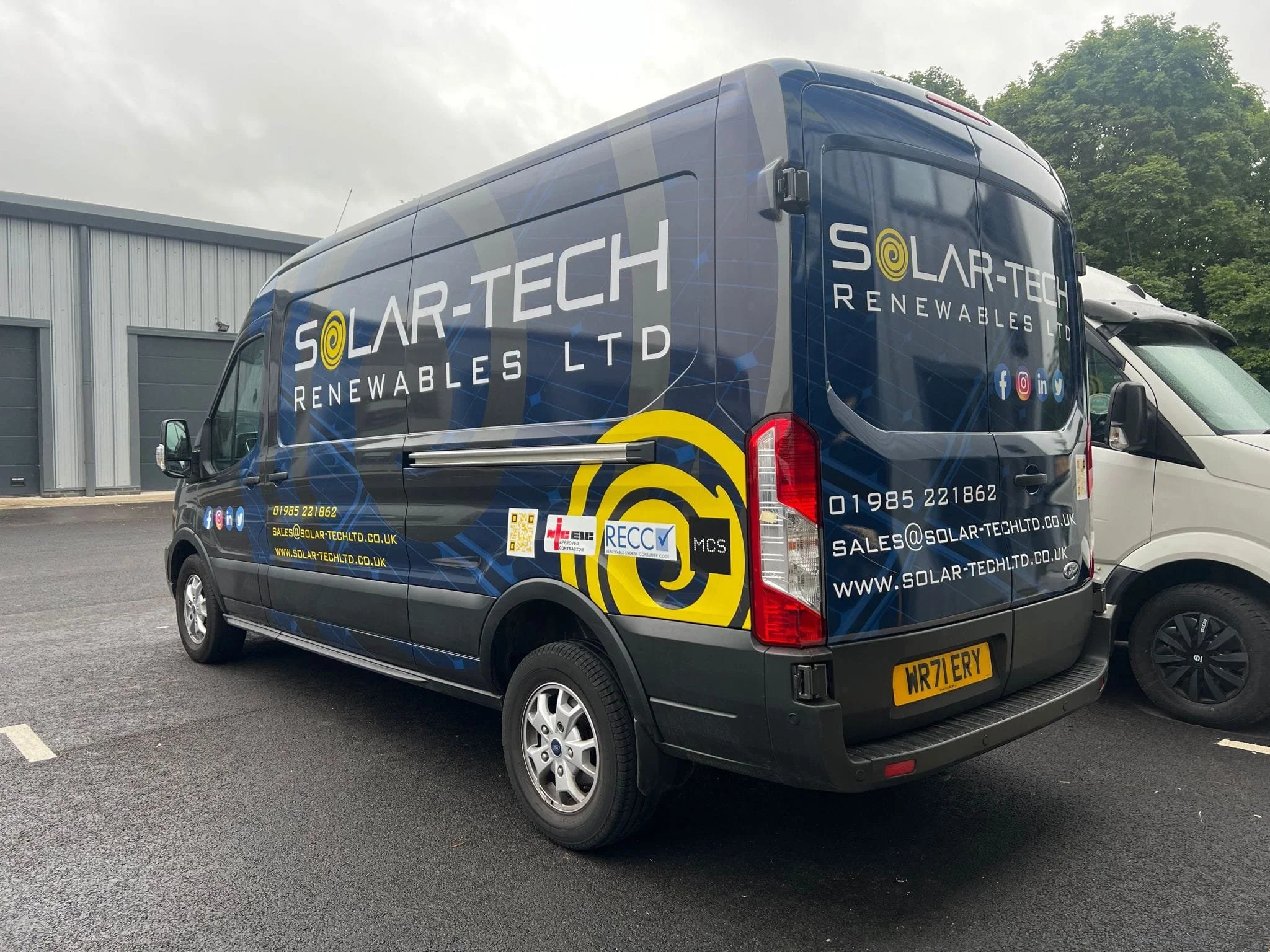 Company van for Solar-Tech Renewables Ltd featuring blue, yellow, and white branding, contact details, and social media icons, parked next to another vehicle in a parking lot.