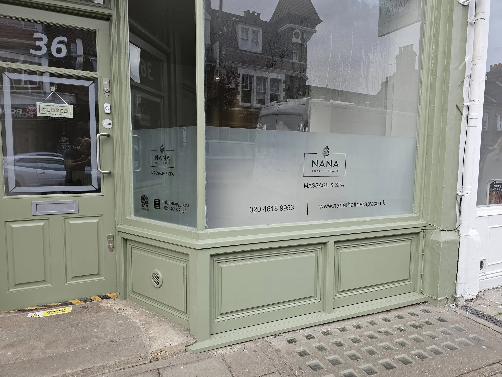 Green storefront with glass window and door, advertising Nana Thai Therapy Massage & Spa, with contact info and website, and a 