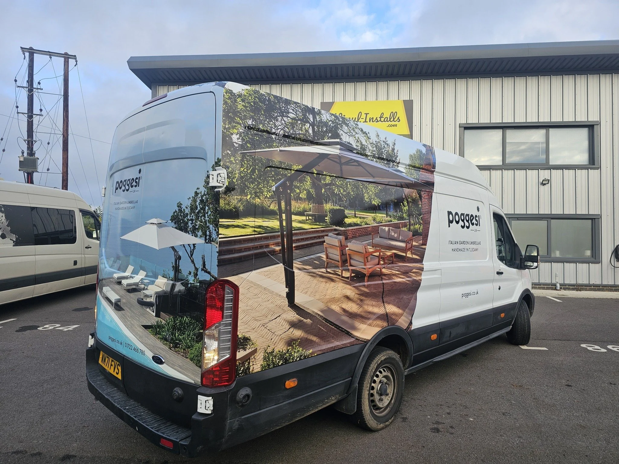 A delivery van with a large wraparound advertisement featuring an outdoor patio scene with outdoor furniture, a pergola, and lush greenery.