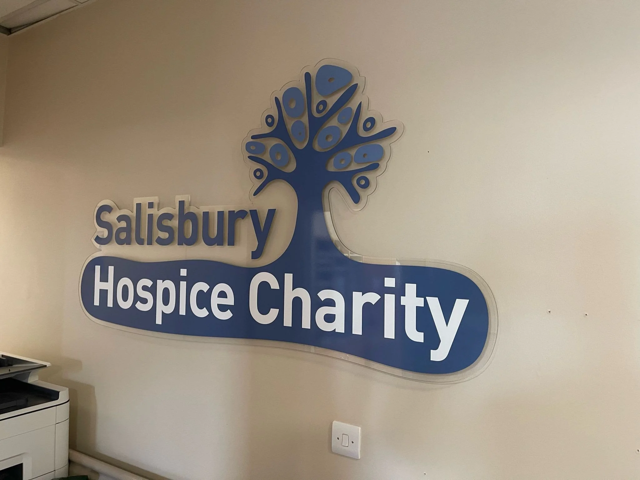 Sign on a wall reading 'Salisbury Hospice Charity' with a stylized blue tree logo.