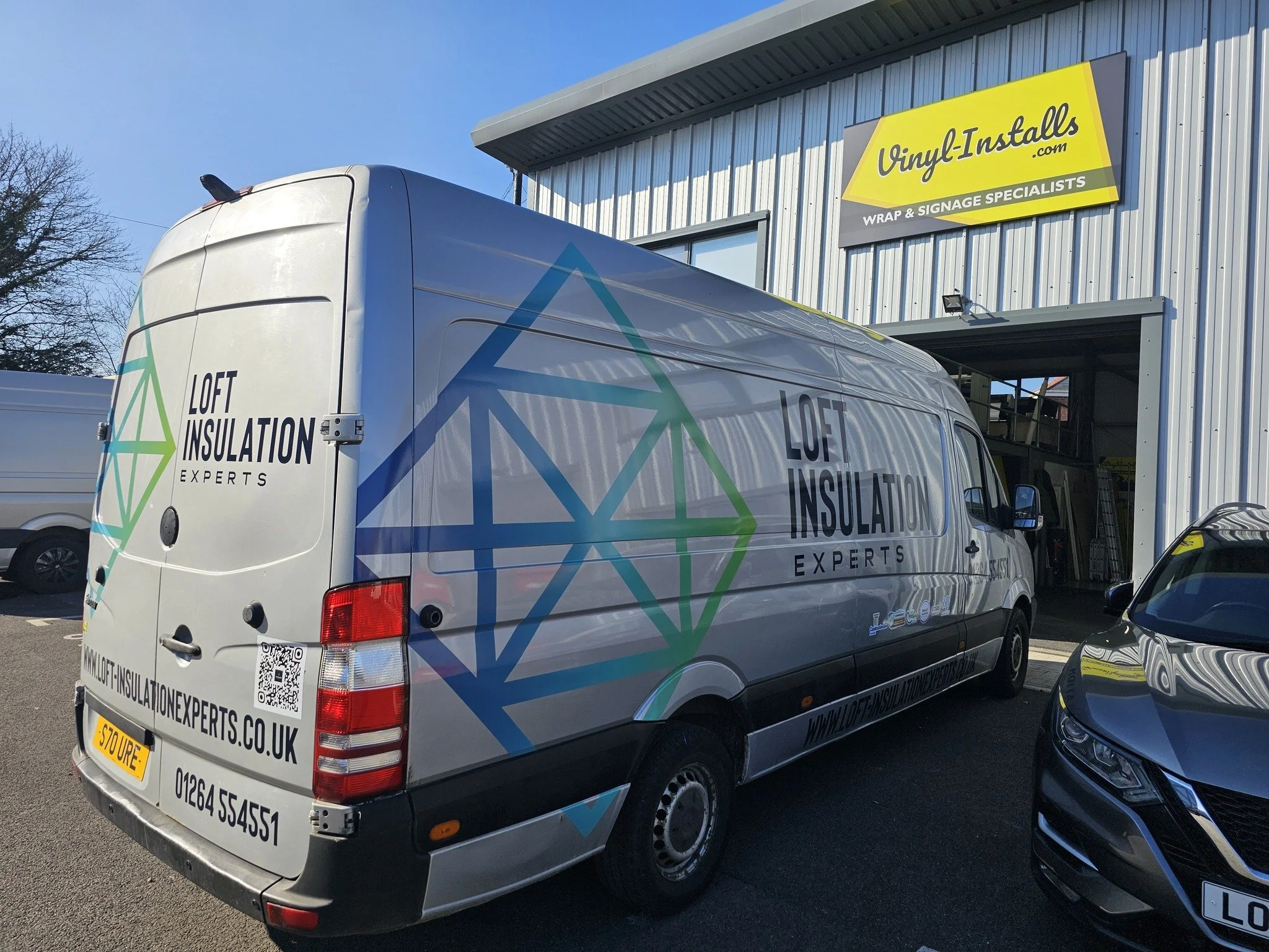 A company van for Loft Insulation Experts parked outside a building with a yellow and gray Vinyl-Installs sign.