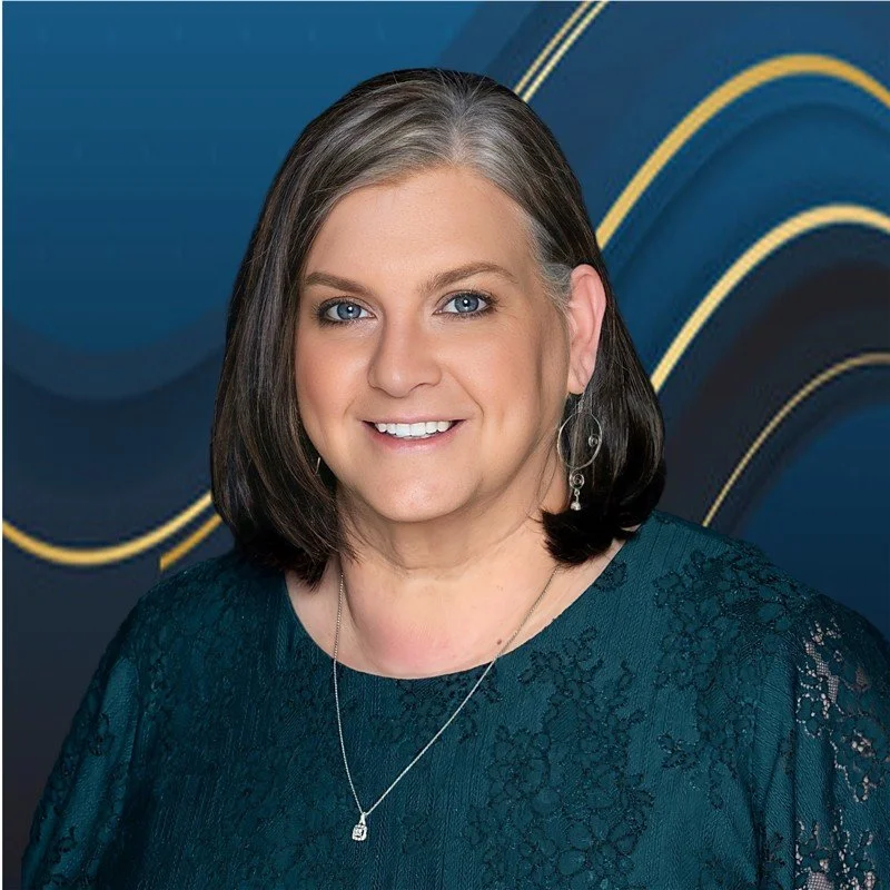 A woman with shoulder-length dark hair wearing a teal lace dress, standing in front of a blue background with gold, curving lines, smiling at the camera.