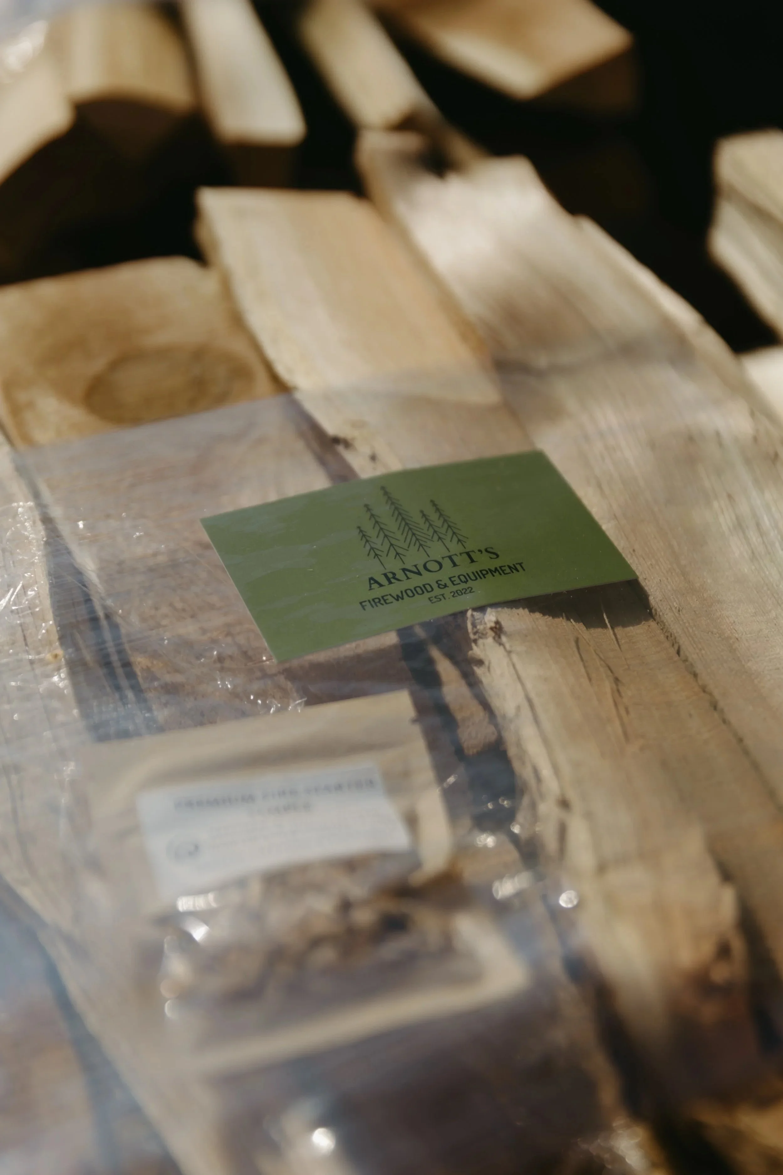 Close-up of firewood logs in a pile with a green label from Arnott's Firewood & Equipment.