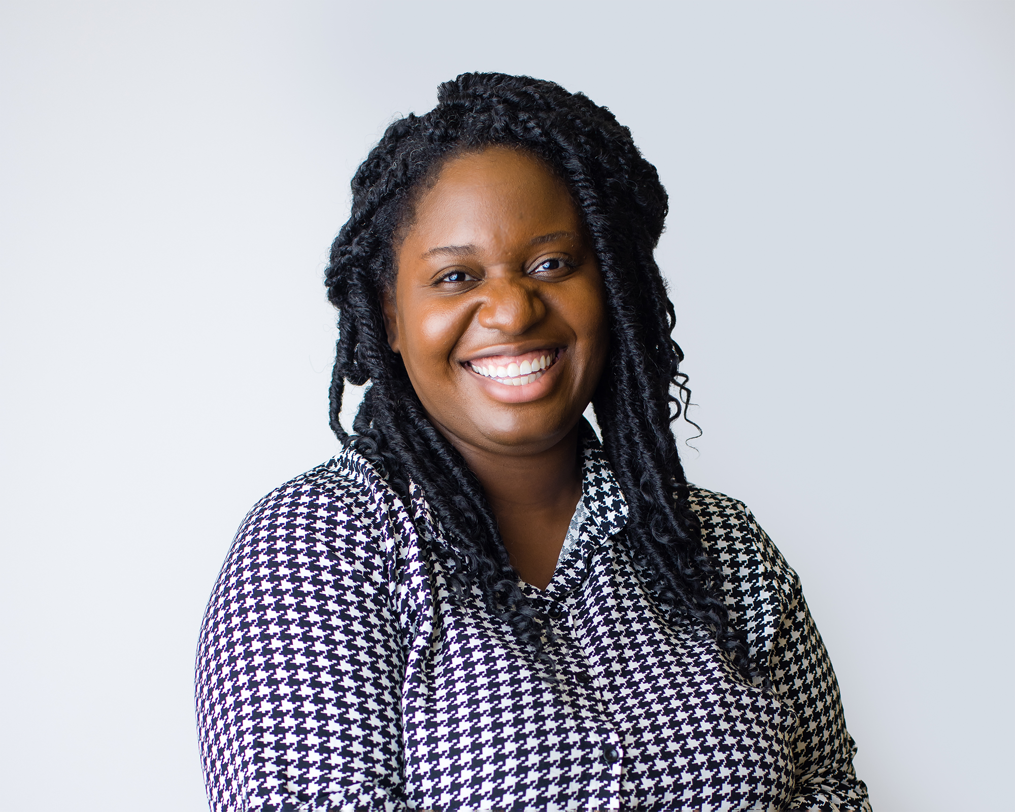 Smiling African American woman with long curly hair wearing a black and white houndstooth pattern shirt.