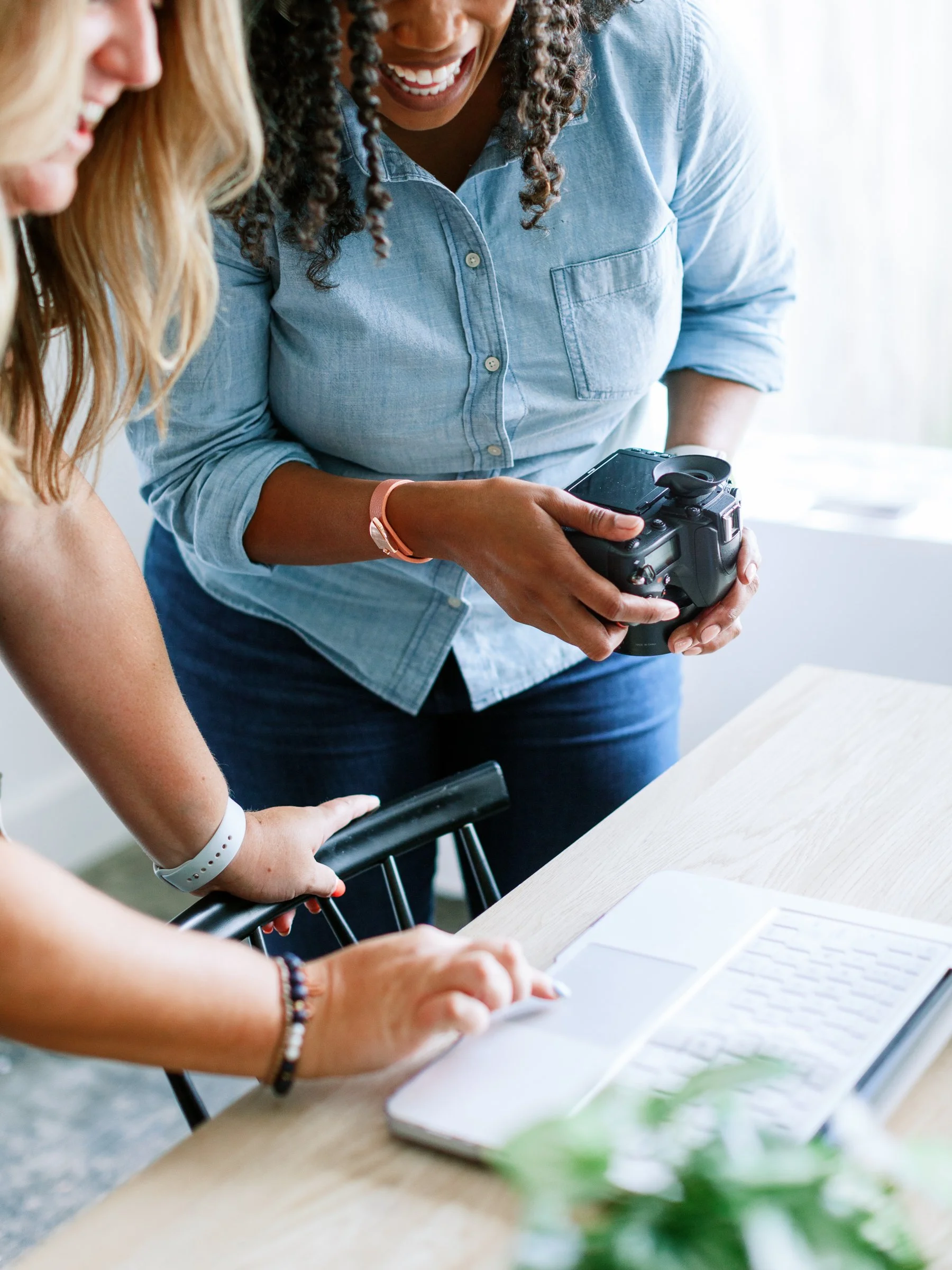 Two women looking at a camera and a laptop on the table.