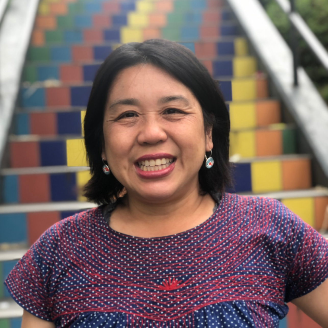 Woman smiling in front of rainbow-colored stairs.