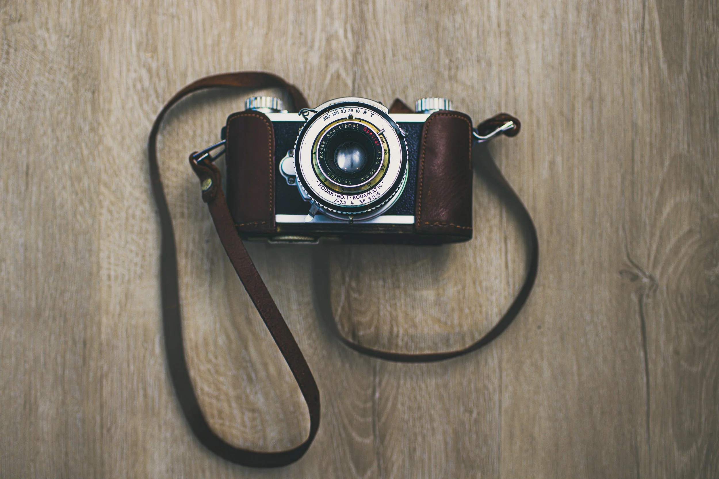 A vintage camera with a leather case and strap resting on a wooden surface.