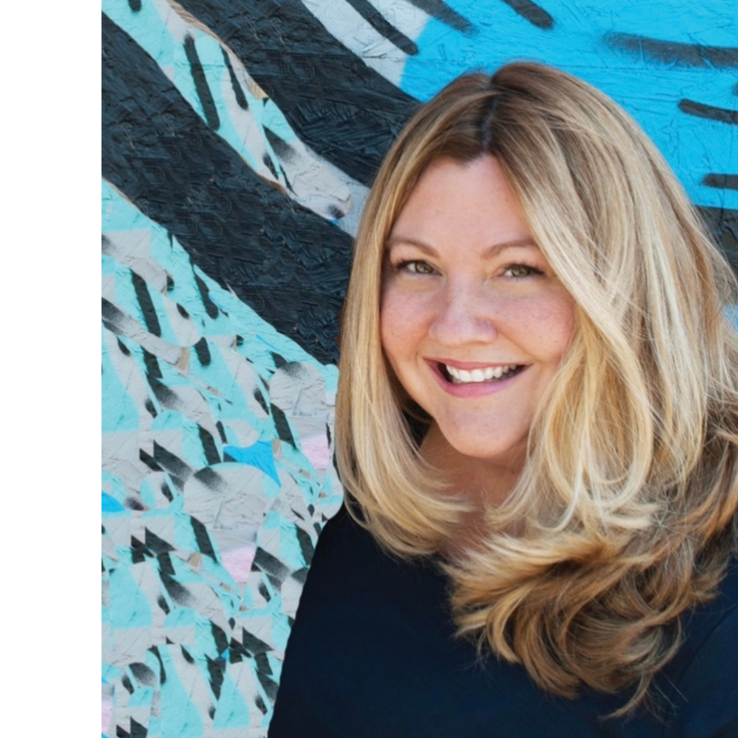 A smiling woman with long blonde hair standing in front of a colorful abstract mural.