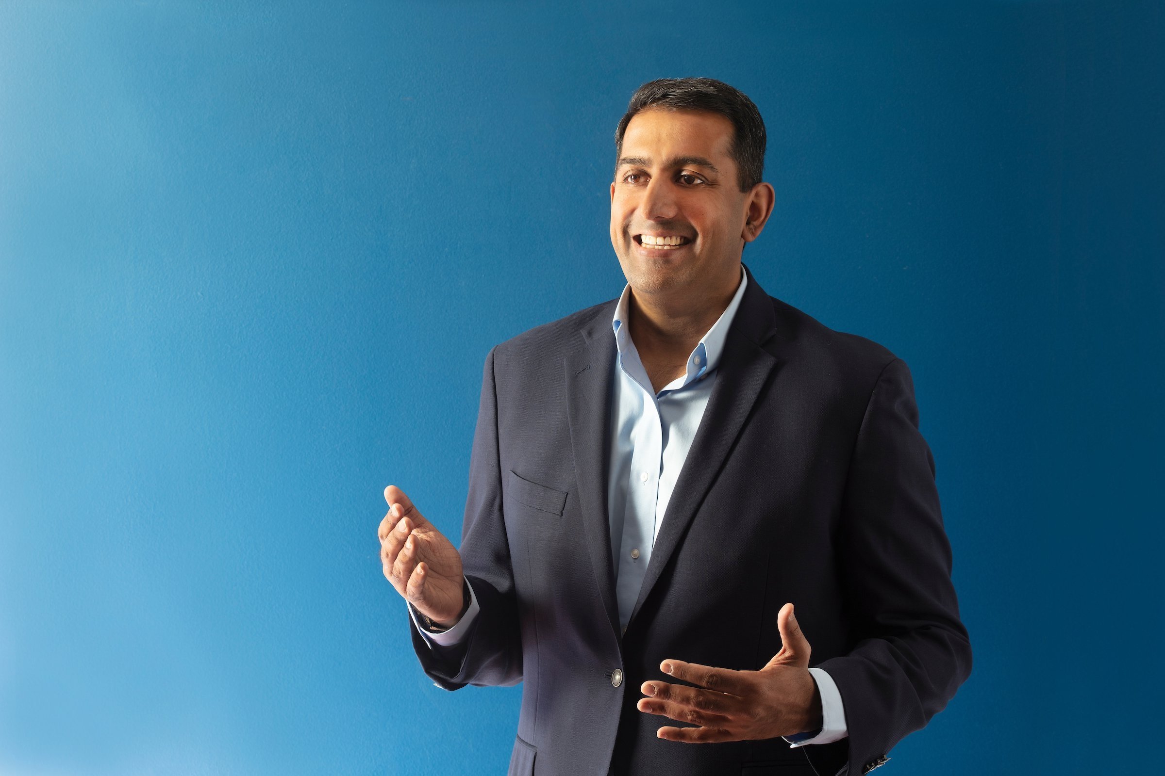 Arvind Venkat stands in front of a blue background. 