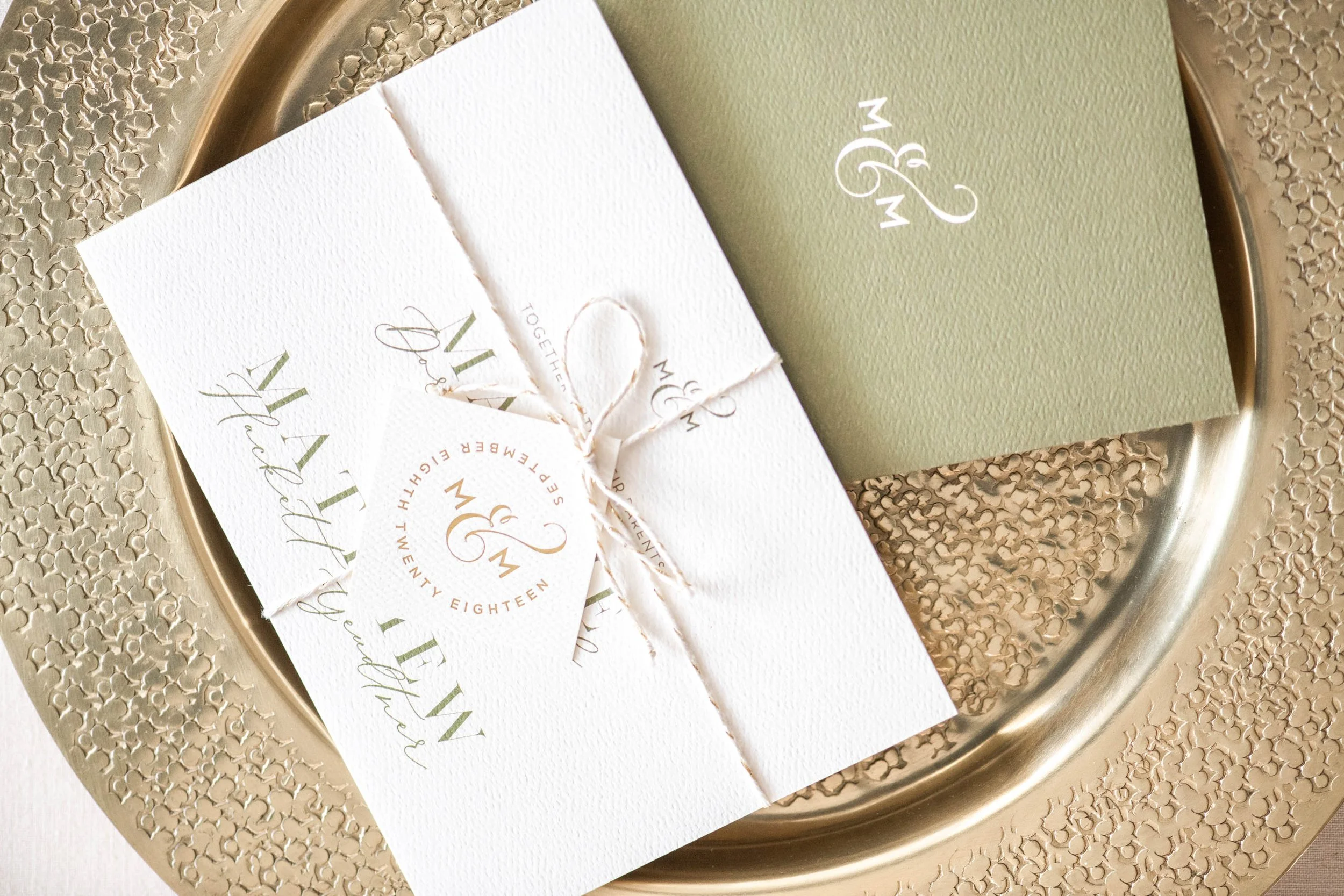 Elegant wedding invitation set with embossed details on gold tray; includes cards and twine with monogram 'M & M,' date September Eight, Twenty Eighteen.