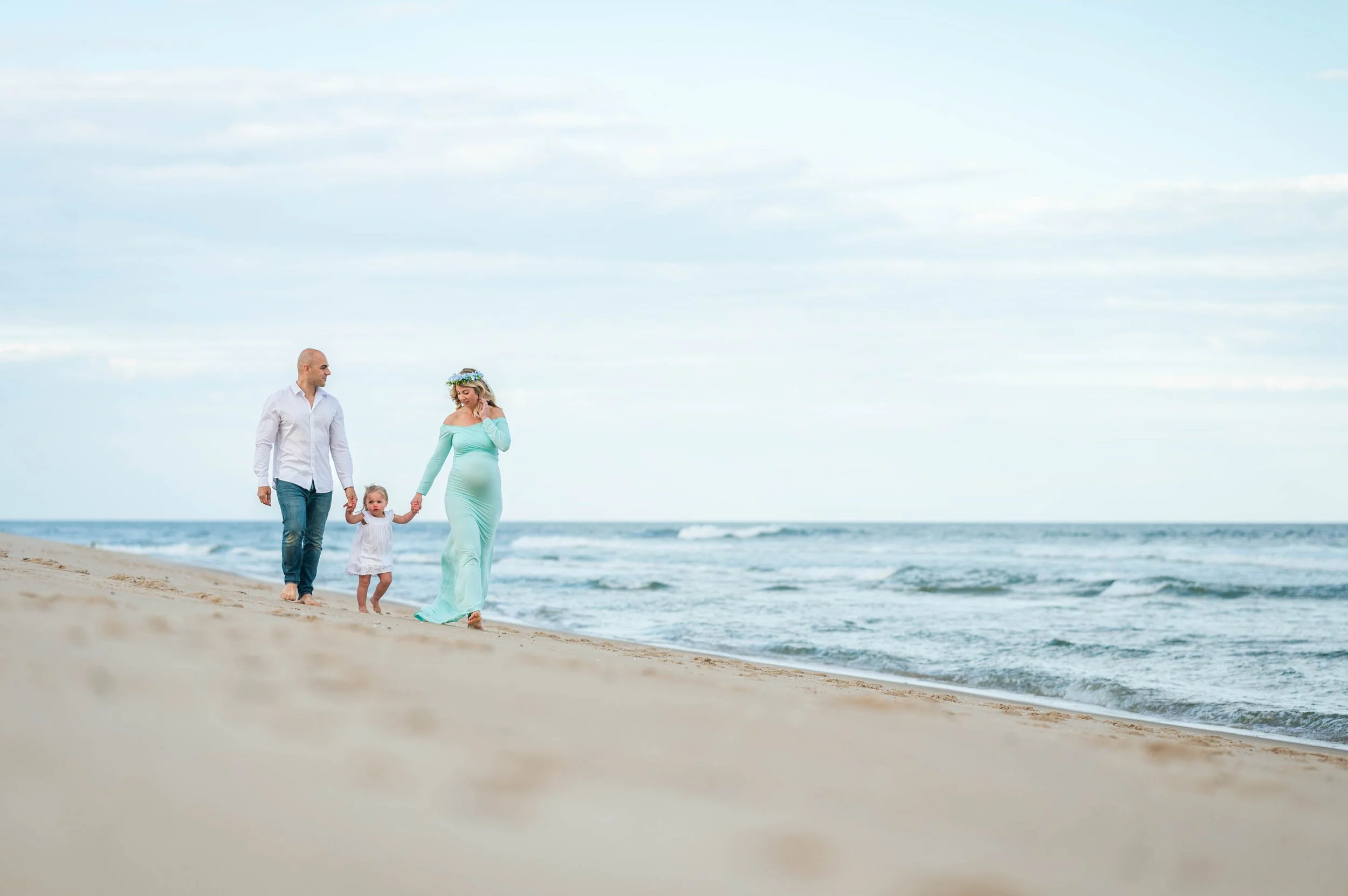 Family walking on beach, pregnant woman, man, child, ocean in background.