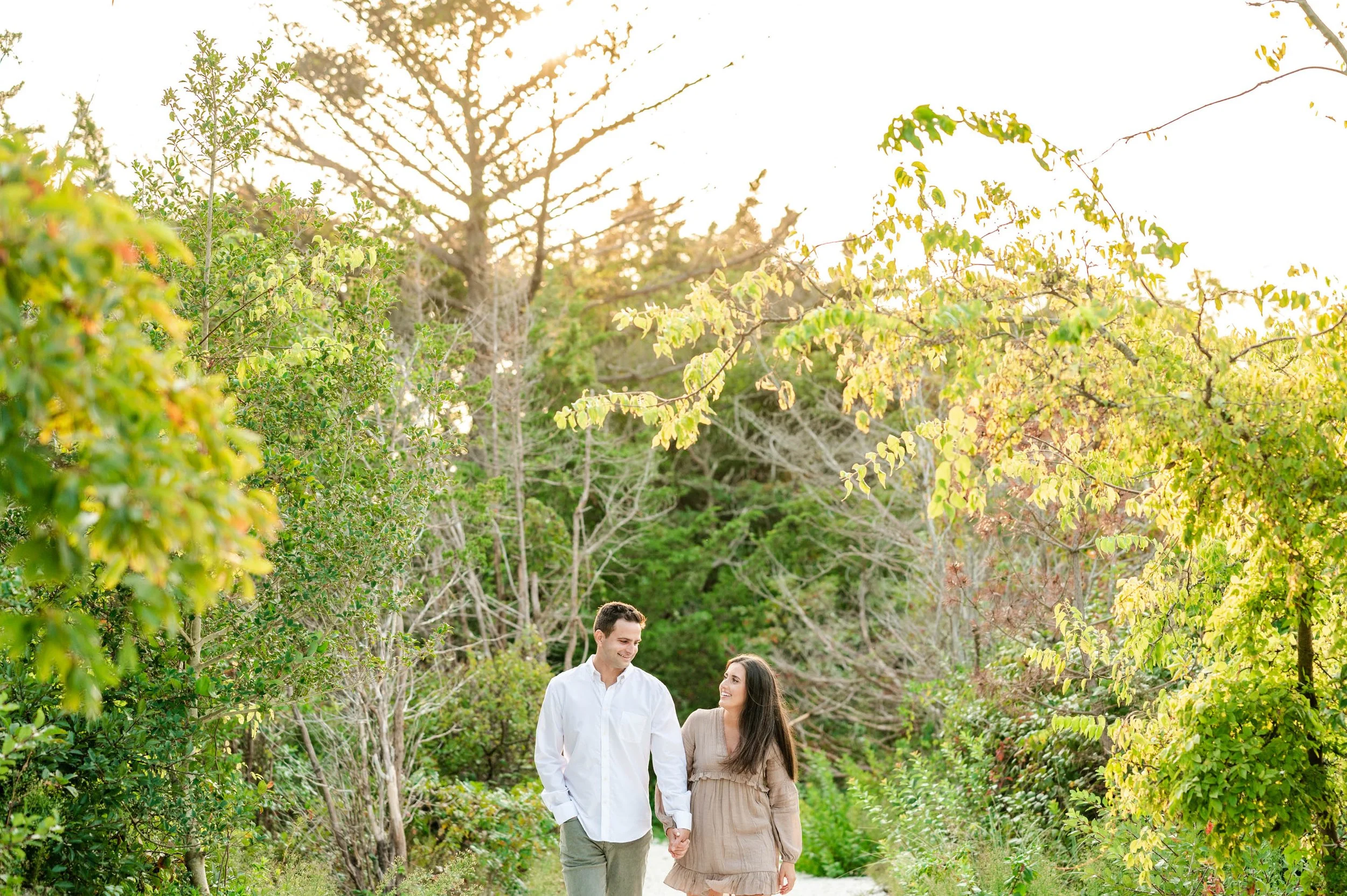 Couple walking hand in hand on a forest path surrounded by green trees during daytime.