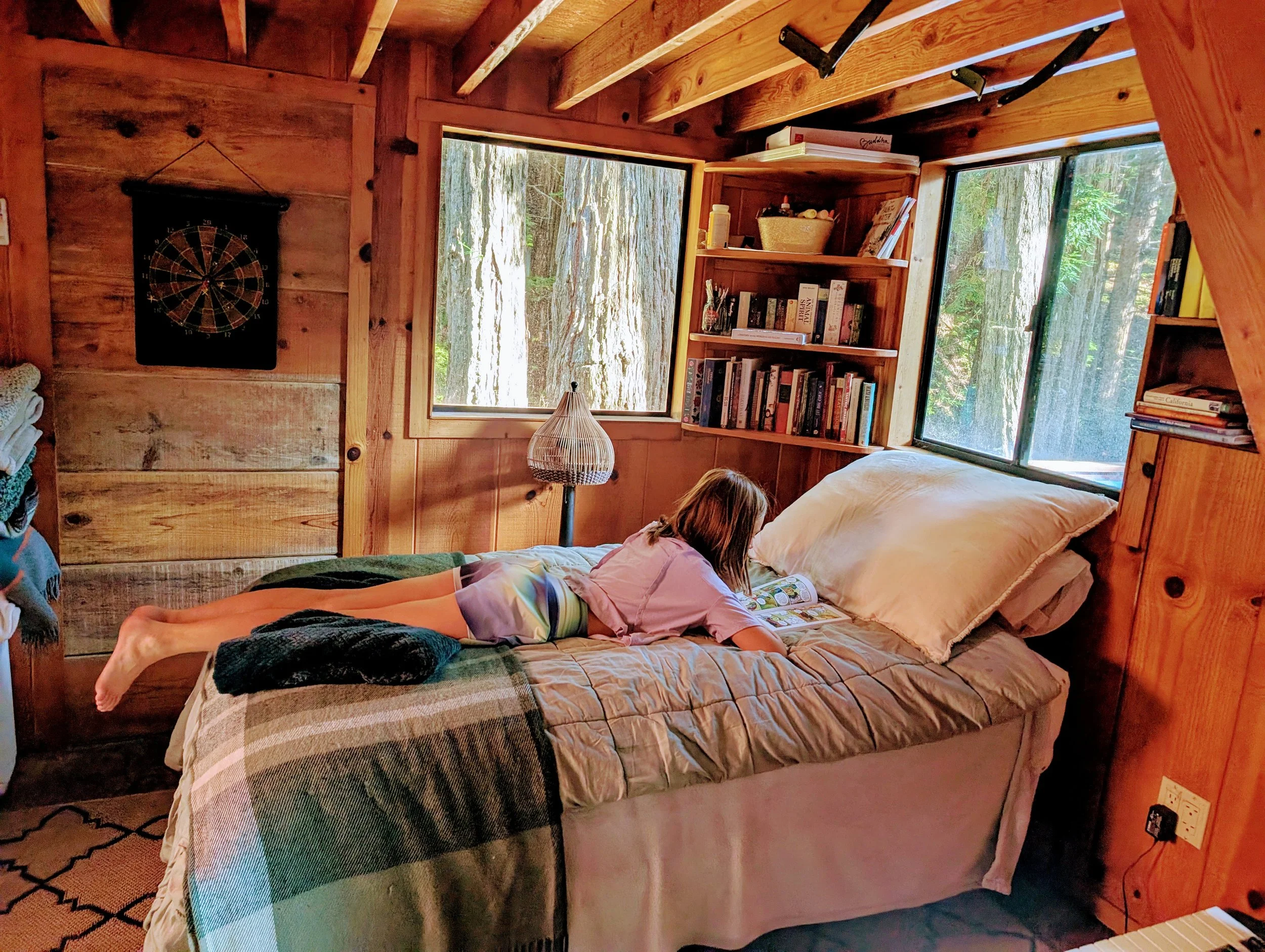 girl reading bed cabin trees