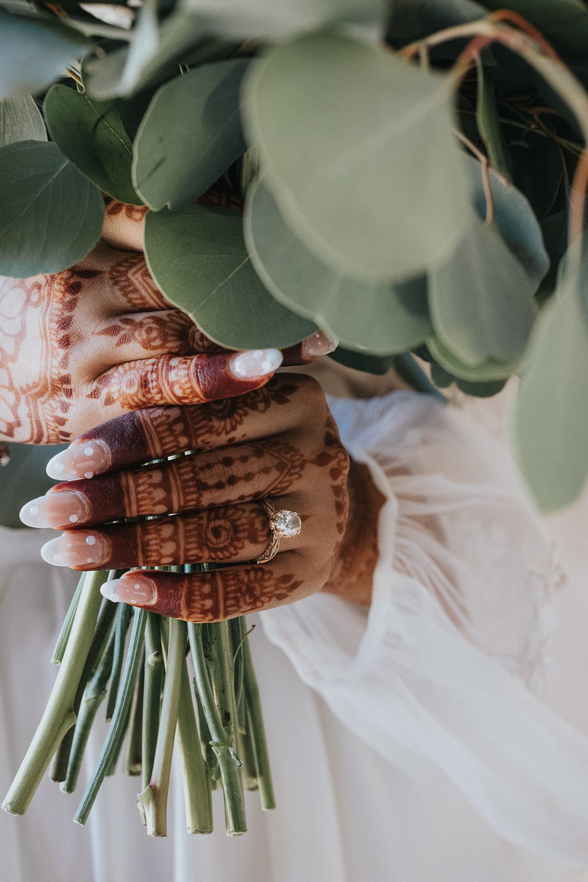    Detail photograph of a bride's hands delicately holding her floral bouquet, showcasing the intricate designs and vibrant colors by Moments by Frank.   
