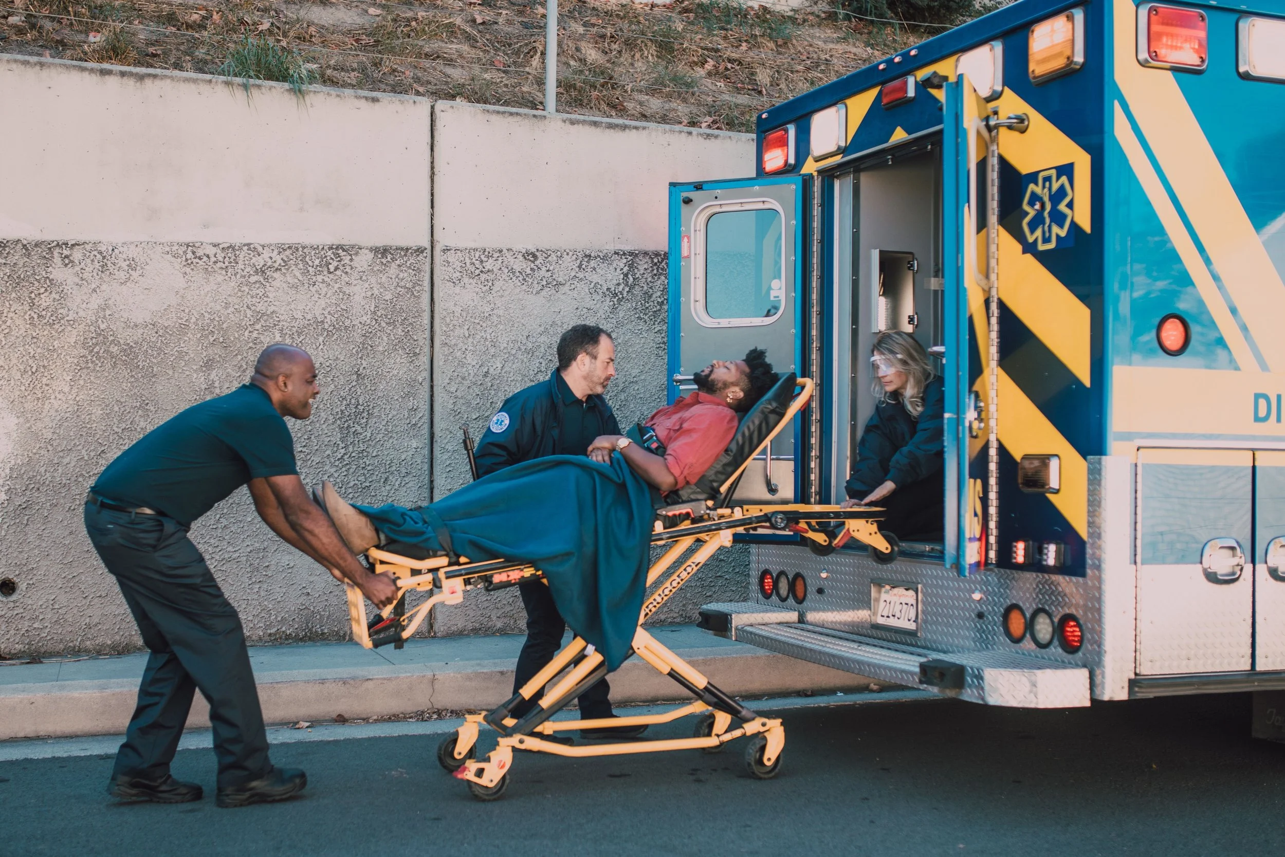Two emergency responders roll a man on a gurney into an ambulance