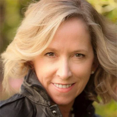 Close-up of a smiling woman with blonde hair outdoors.